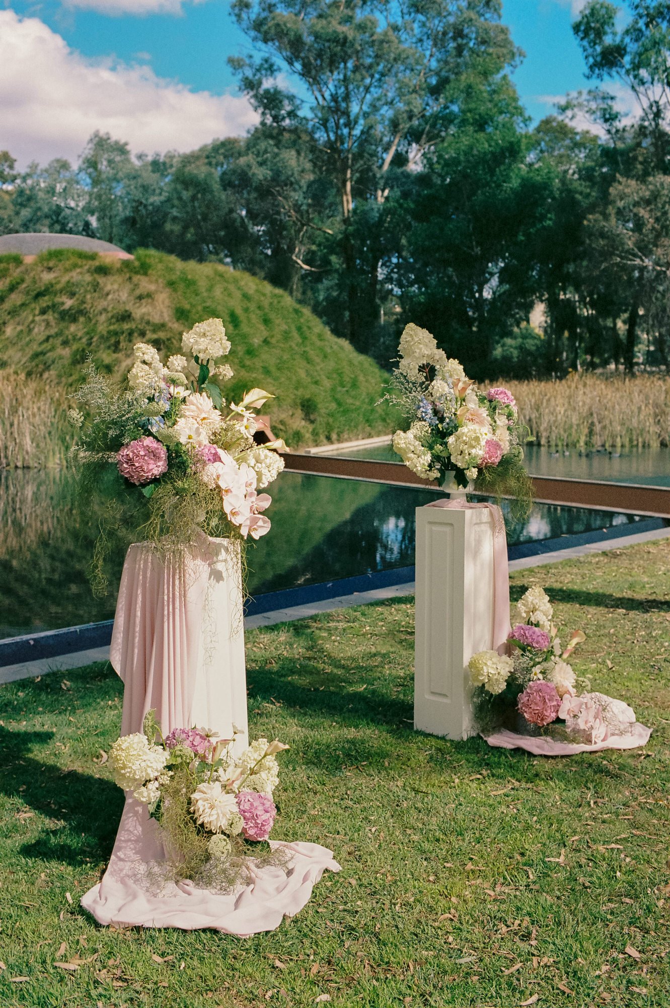 Elegant floral arrangements with pastel hydrangeas and orchids styled beside the water at a National Gallery of Australia wedding in Canberra, photographed on 35mm film by Corinna & Dylan, editorial wedding photographers