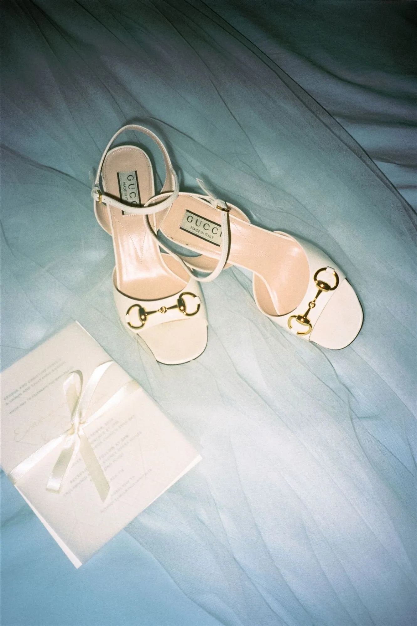 Elegant Gucci bridal shoes styled with a ribbon-tied wedding invitation on soft blue tulle, photographed on 35mm film by Corinna & Dylan for a Sydney Opera House wedding, editorial wedding photographers