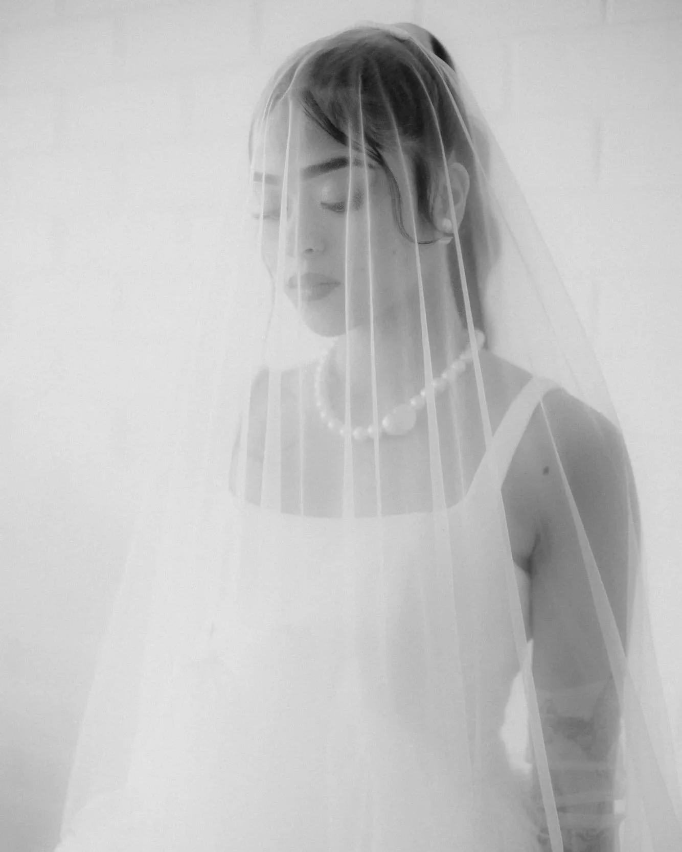 Black and white portrait of a bride in soft light, wearing a pearl necklace and veil, with a serene expression