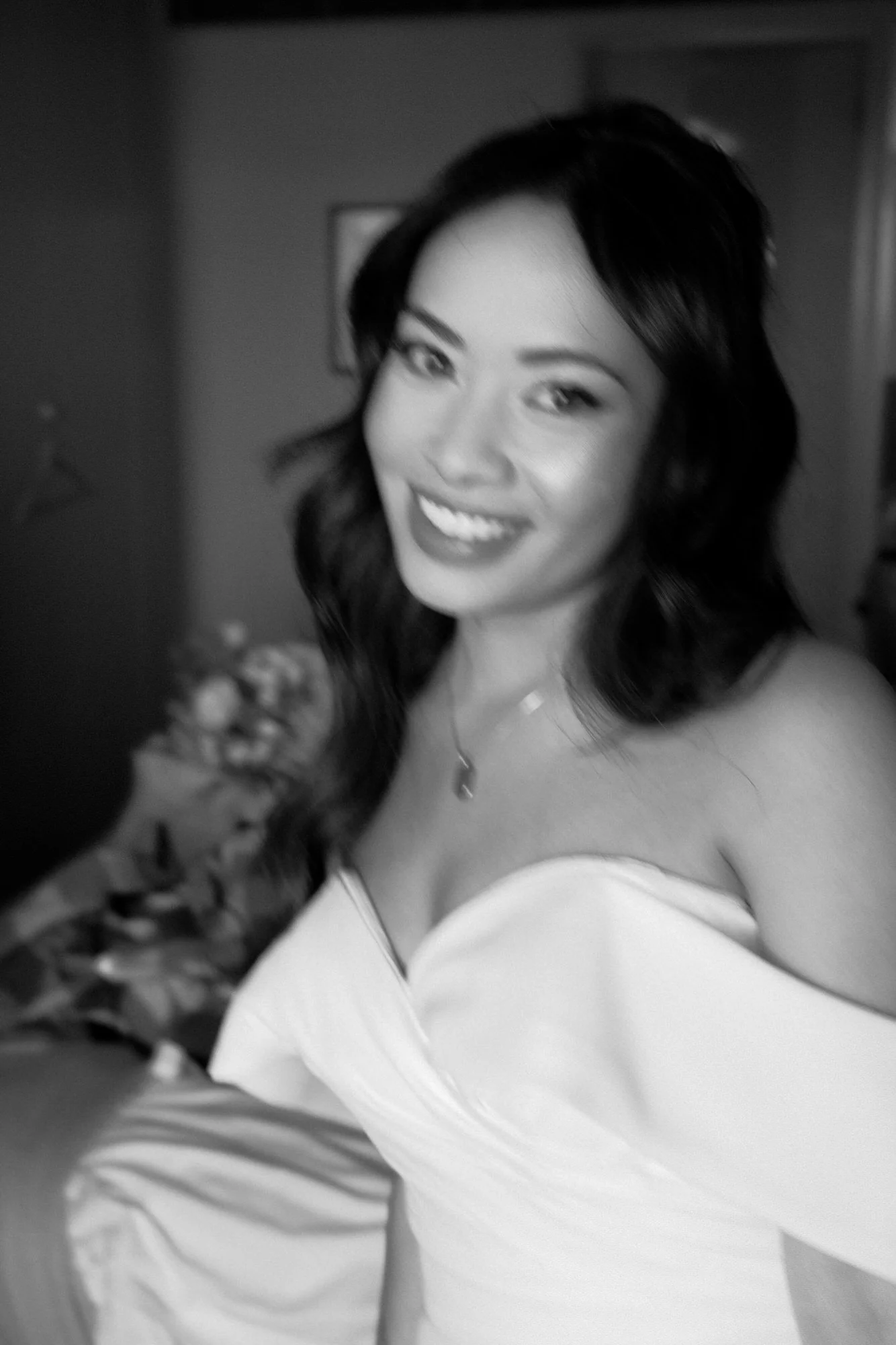 Bride smiling in an off-the-shoulder gown, captured in soft motion blur before the ceremony, creating a dreamy, intimate feel. Digital