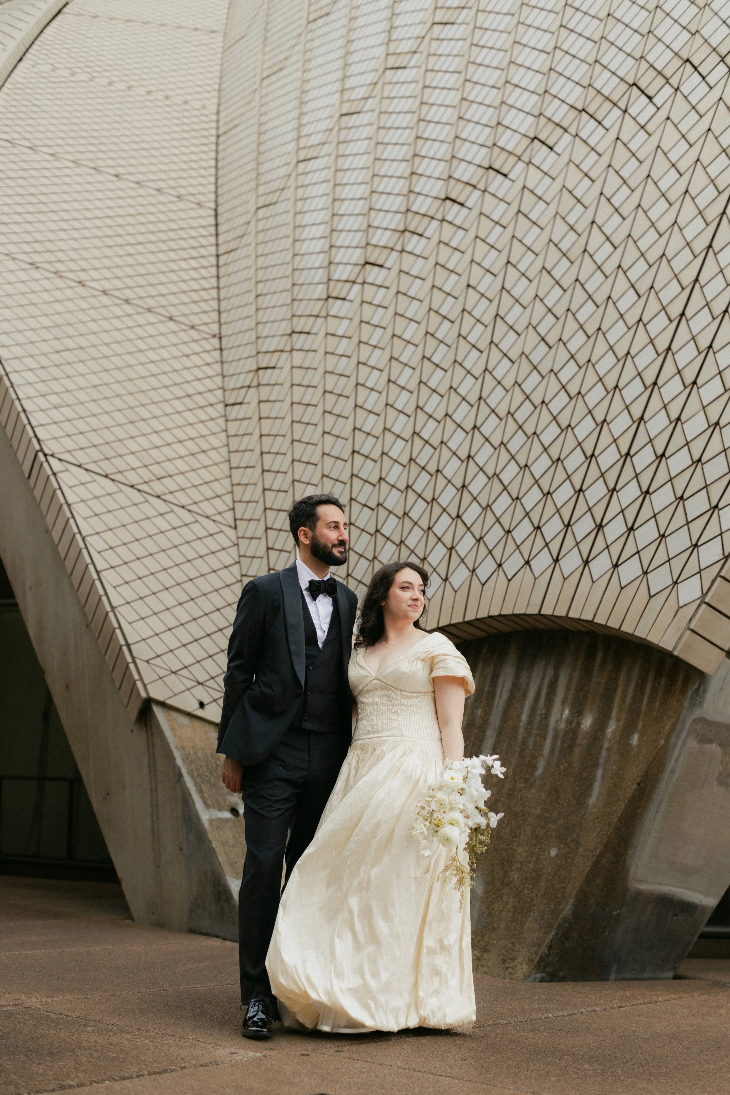 Bride holding a bouquet and groom in a black suit outside the Sydney Opera House on their wedding day