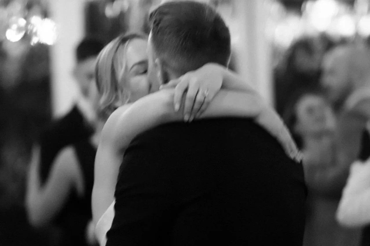 Bride and groom sharing a kiss during their first dance at Poachers Pantry wedding, captured in soft black and white by Corinna & Dylan, modern wedding photographers.
