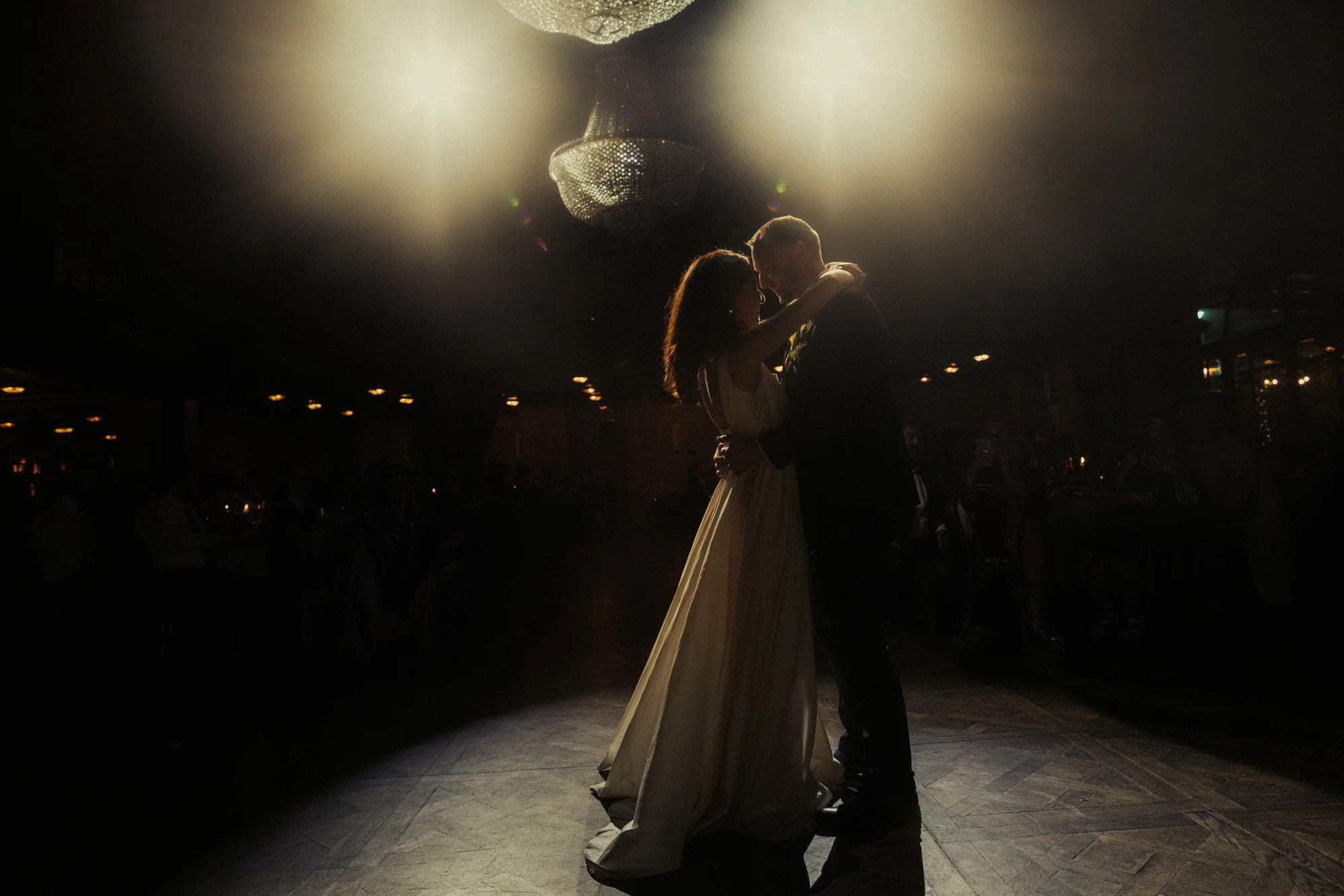 Bride and groom sharing their first dance beneath chandeliers at The Grounds of Alexandria wedding reception in Sydney, captured in cinematic low light by Corinna & Dylan, modern wedding photographers