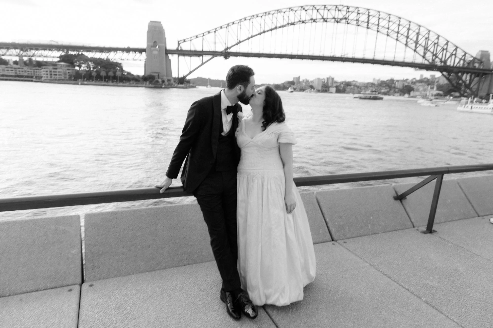 Newlyweds kiss by Sydney Harbour with the Opera House and Sydney Harbour Bridge as backdrop, captured by Corinna & Dylan