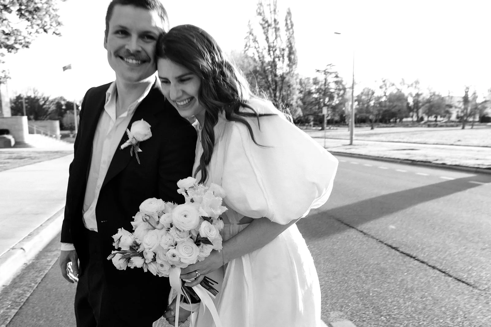 Black and white candid of a couple during their Canberra elopement, laughing together while walking with a bouquet.