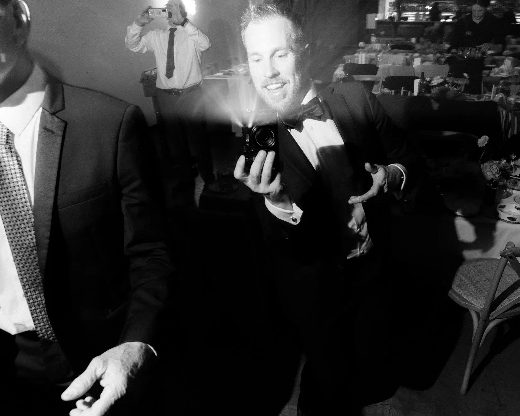 Documentary wedding photography in Canberra — a candid black and white shot of a guest capturing the dance floor chaos, camera flash lighting up the night. Real, unscripted moments that make wedding receptions unforgettable.