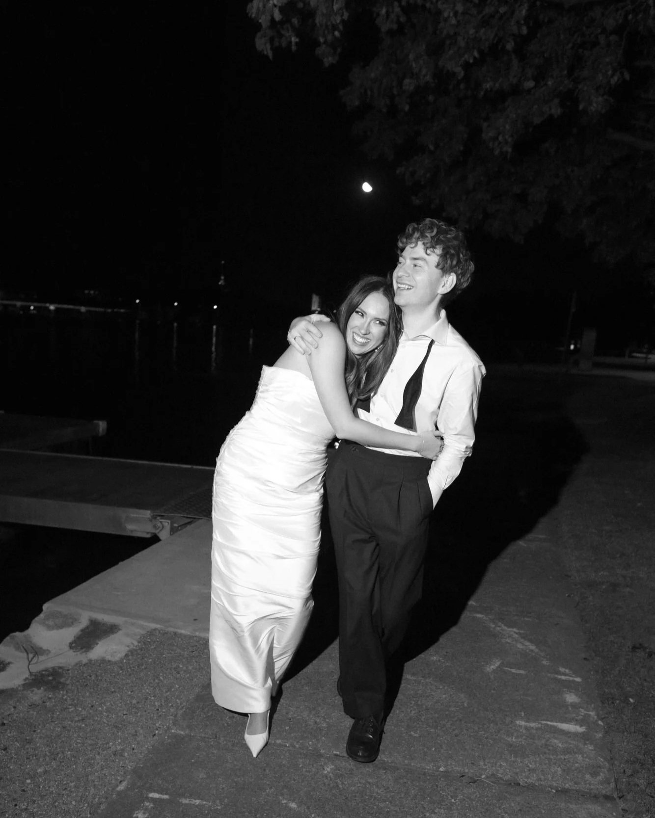 The Boat House wedding — a candid black and white night portrait of the bride and groom walking arm in arm after their reception, full of joy and intimacy