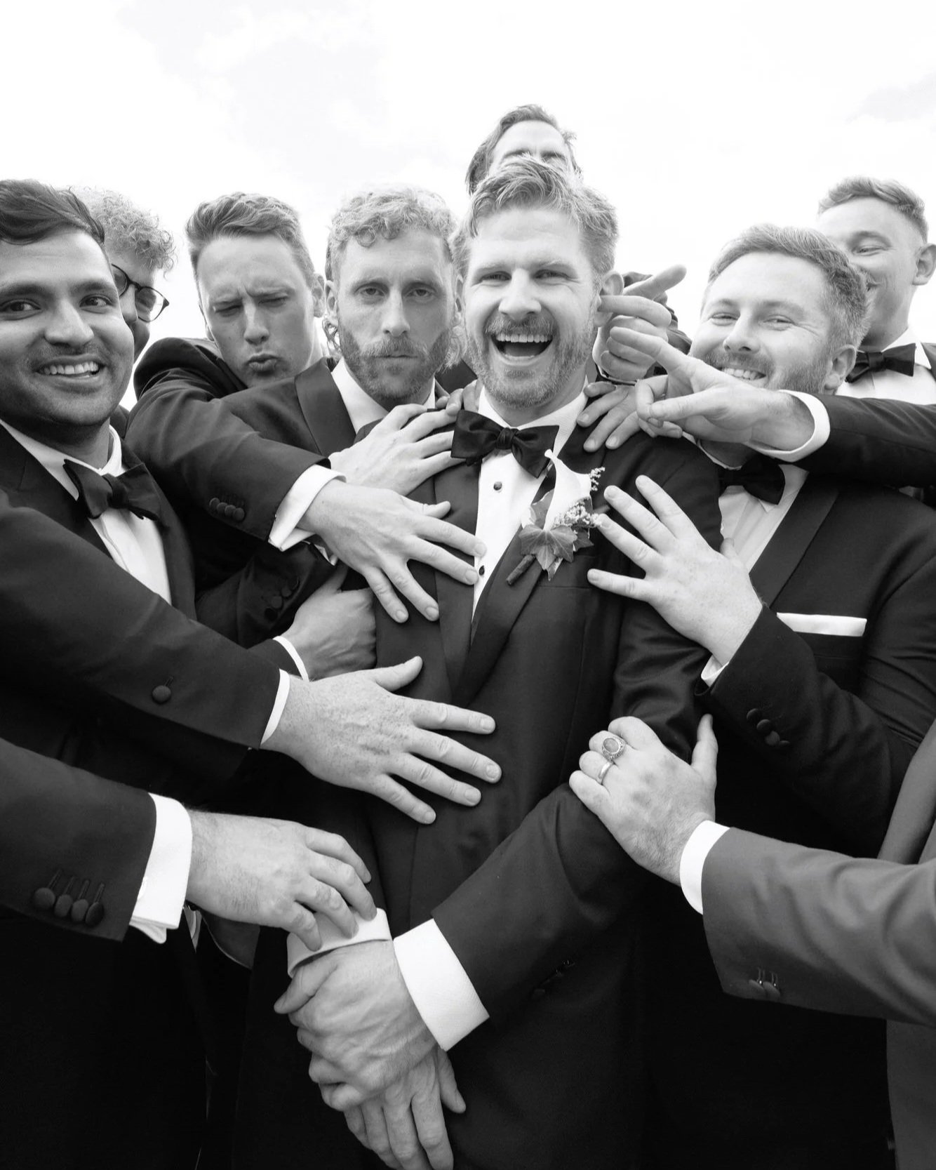 A groom swallowed up in laughter and hands — brotherhood, mischief, and affection all tangled together.