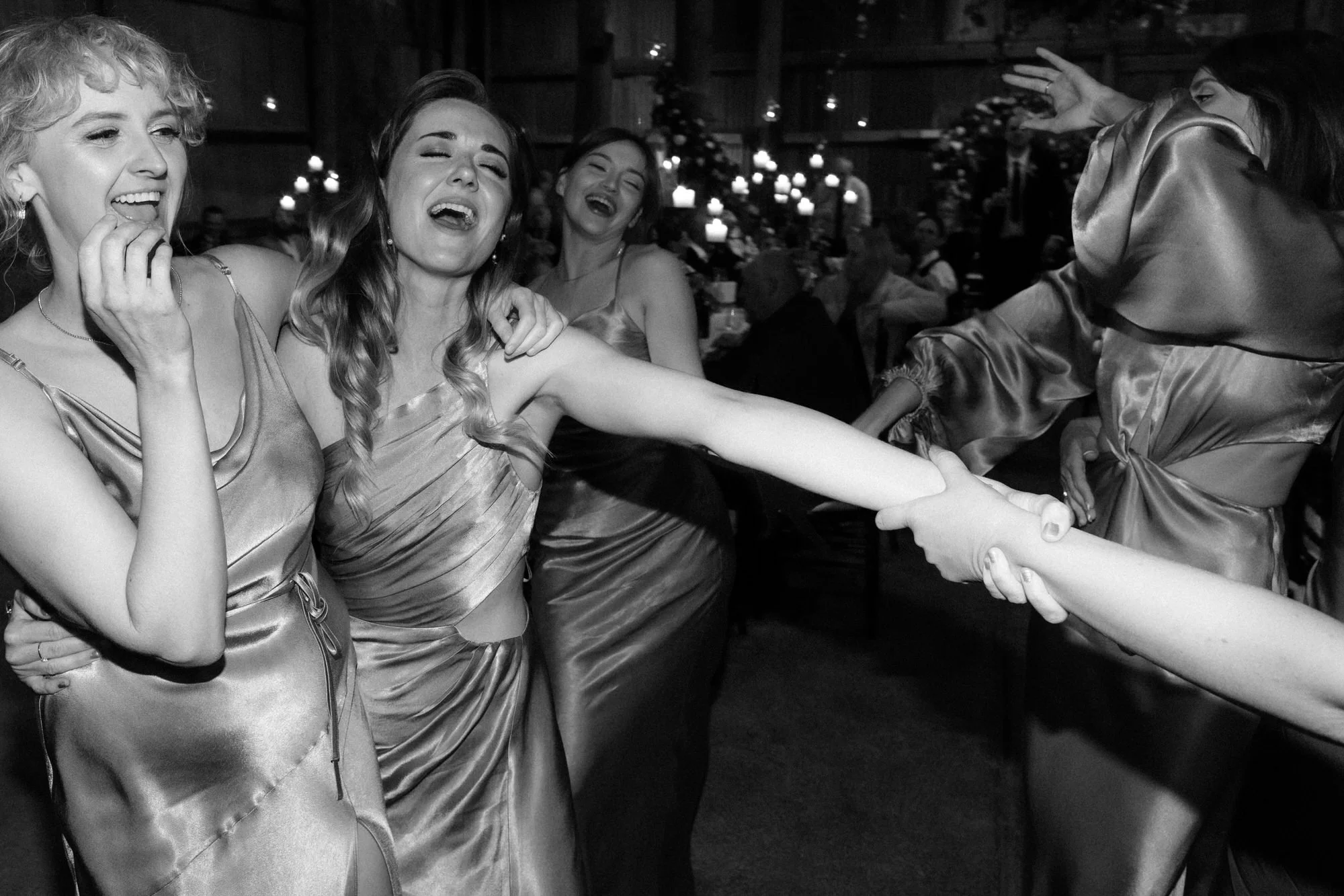 Bridesmaids laughing and dancing together on the wedding reception dance floor, captured in energetic black and white by Corinna & Dylan