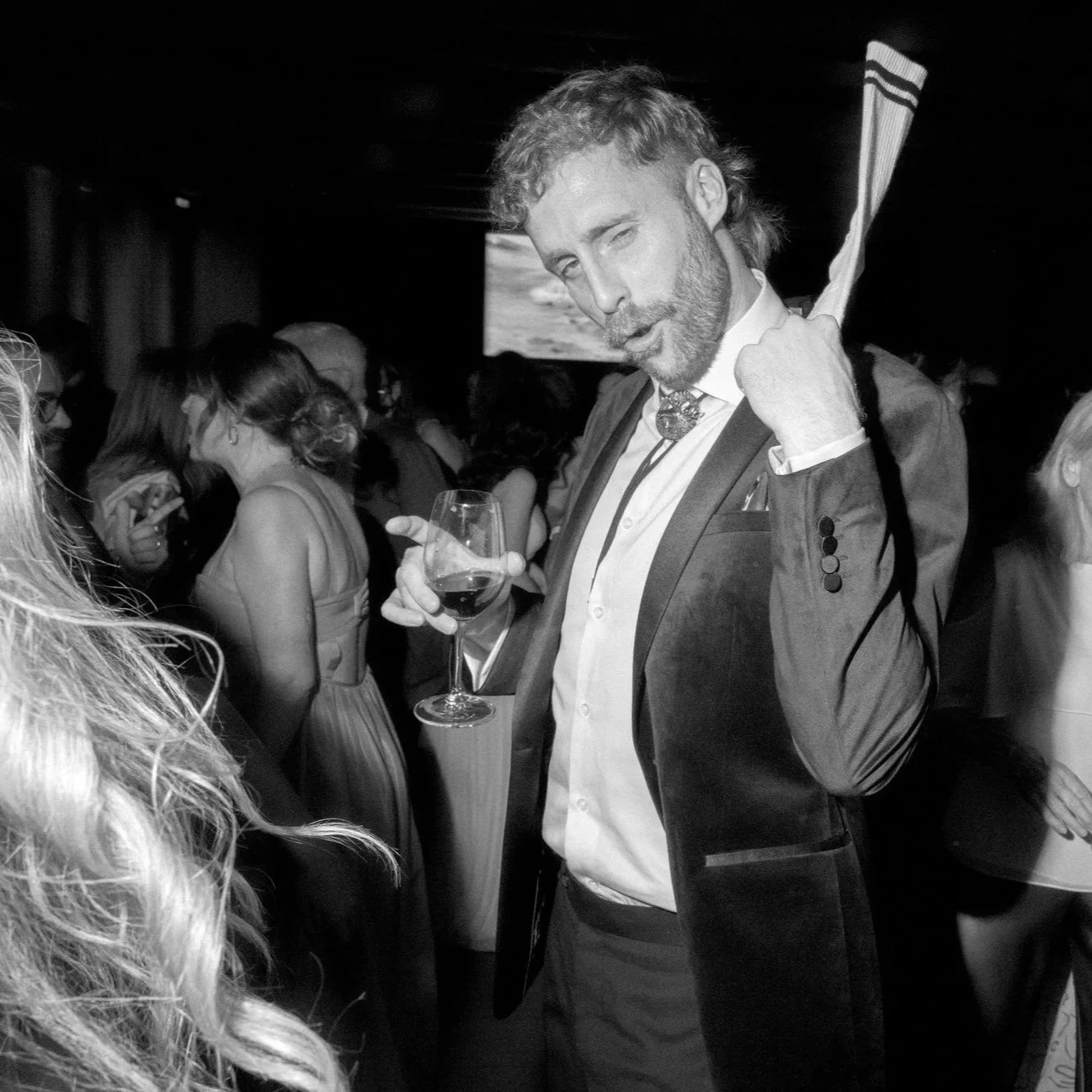 Guest striking a playful pose with a glass of wine on the dance floor during a National Gallery of Australia wedding reception in Canberra, captured in lively black and white by Corinna & Dylan, wedding photographers