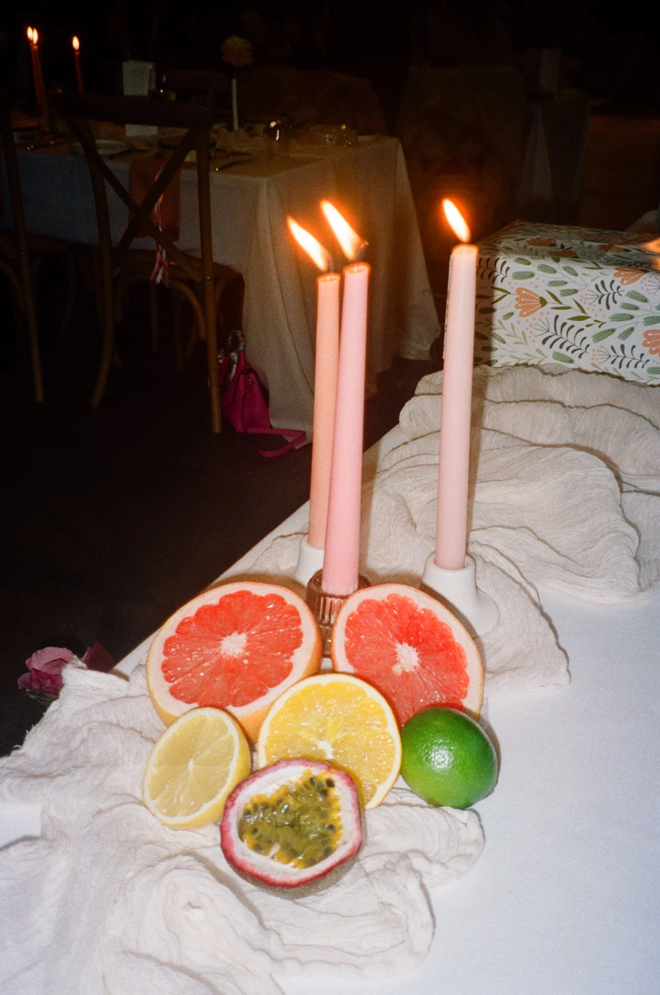 Wedding table detail with sliced citrus fruits, pink taper candles, and linen draping, captured on film at a vibrant Canberra wedding reception by Corinna & Dylan