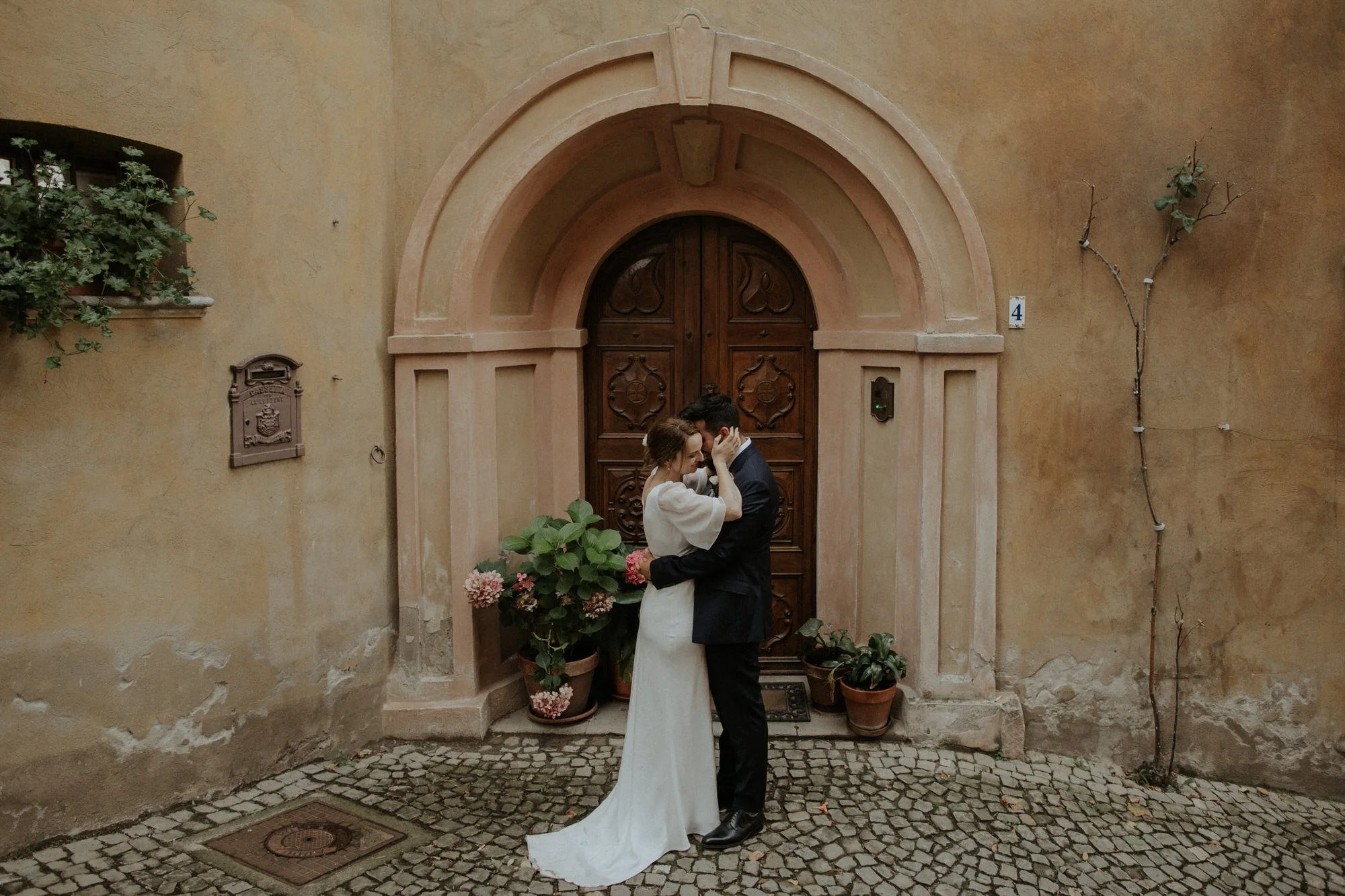 Romantic wedding portrait at Villa Beccaris in Monforte d’Alba, Italy, with the couple embracing beneath an arched doorway, captured by Corinna & Dylan, destination wedding photographers