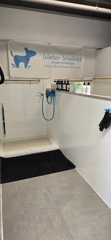One of 2, DIY dog wash bays designed for water walkies hydrotherapy, with a tiled area, water equipment on the walls, and a sign that reads 'Water Walkies Hydrotherapy Fitness Rehabilitation Recovery.'
