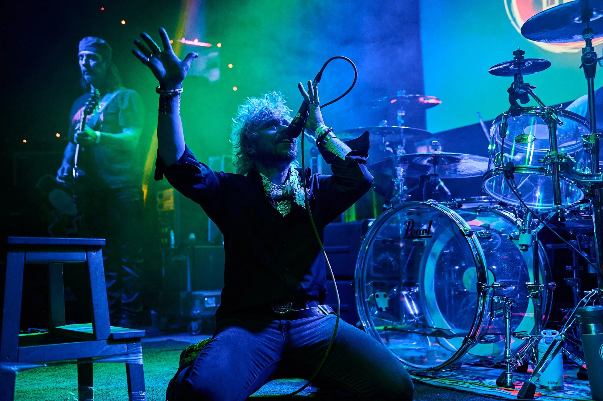 A TK singing on stage on his knees with green and blue lighting.