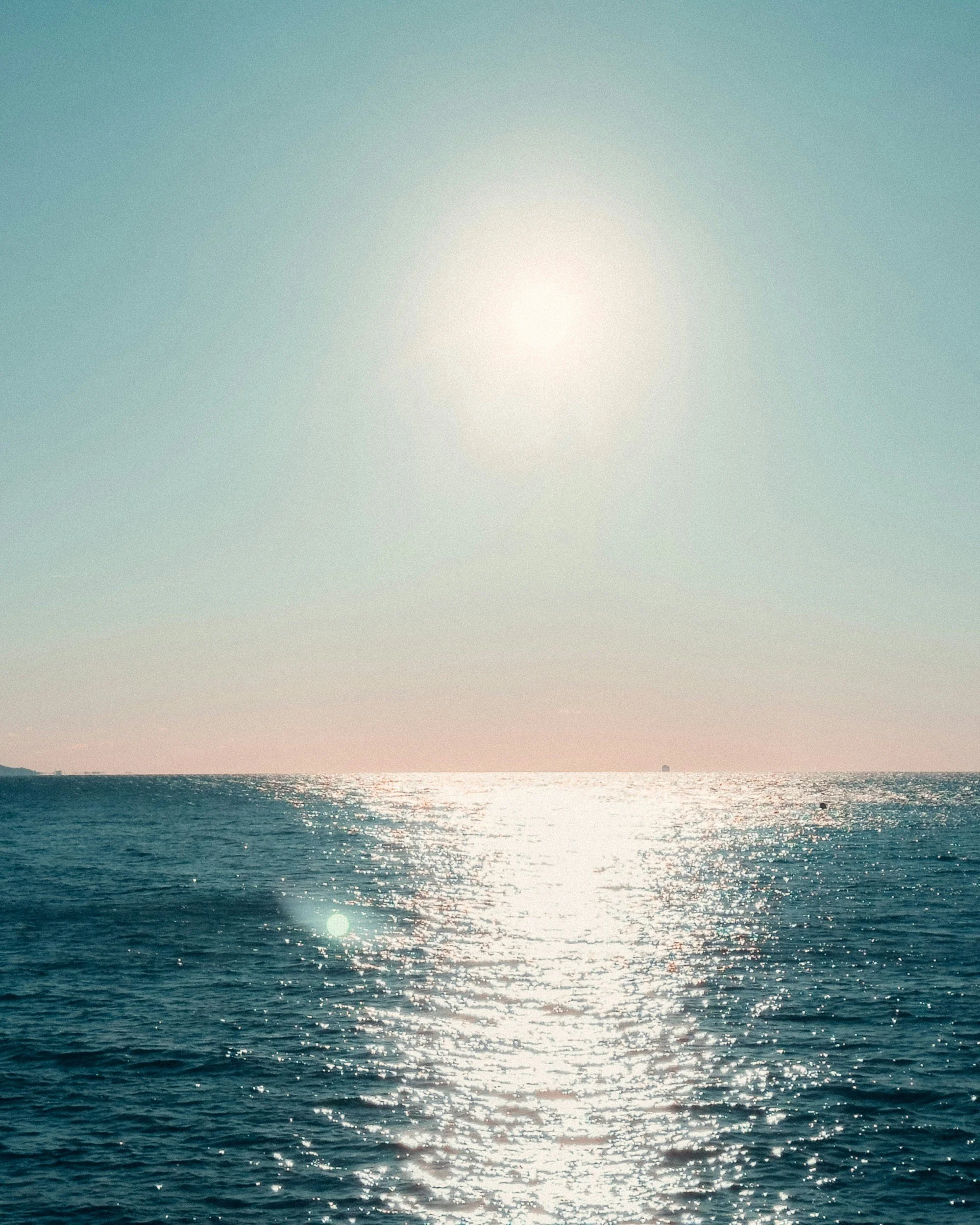 Sun shining over a calm ocean with reflections on the water, horizon line in the distance.