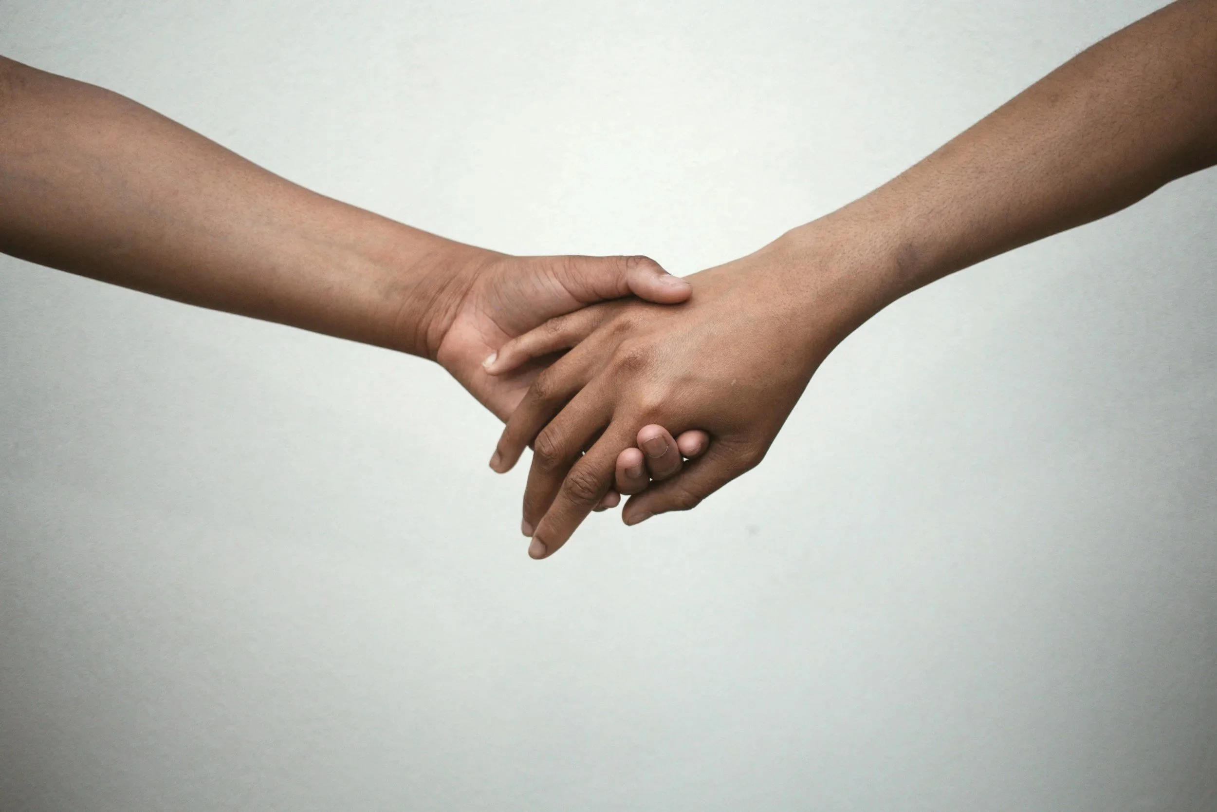 Two people holding hands, one with darker skin and the other with lighter skin, against a plain background.