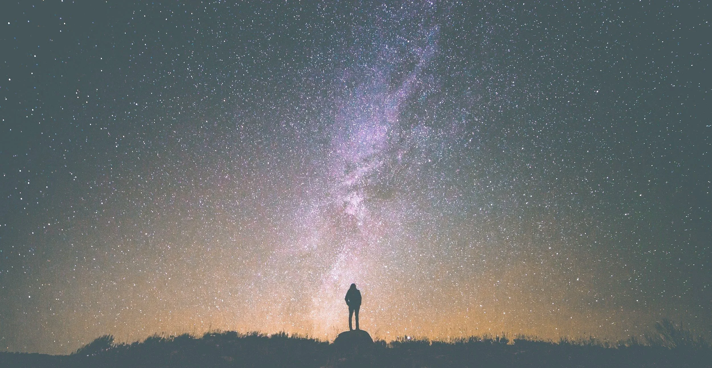 A person standing on a rock, looking at the night sky filled with stars and the Milky Way galaxy.