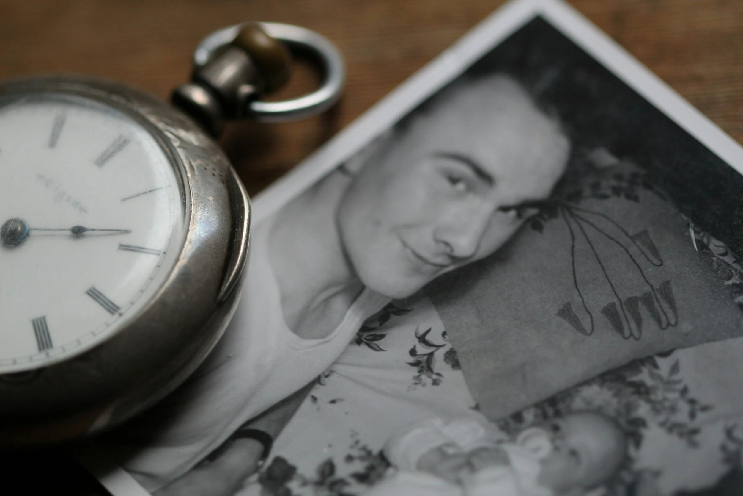 Close-up of a vintage pocket watch and black-and-white photographs, including a smiling woman and a family scene, on a wooden surface.