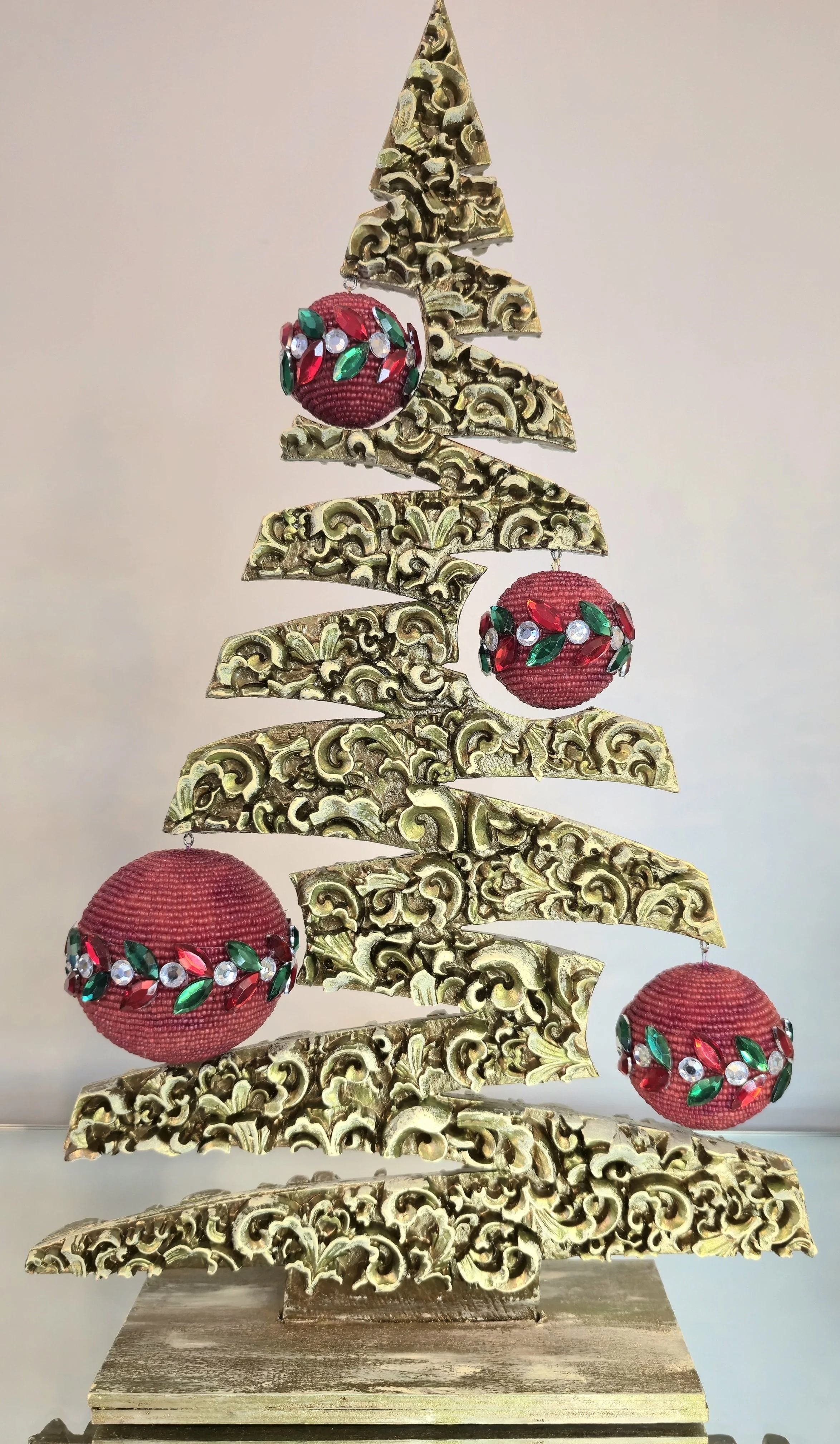 Un arbre de Noël décoratif avec des branches en fil métallique doré et des boules de Noël rouges ornées de pierres vertes, blanches et rouges.