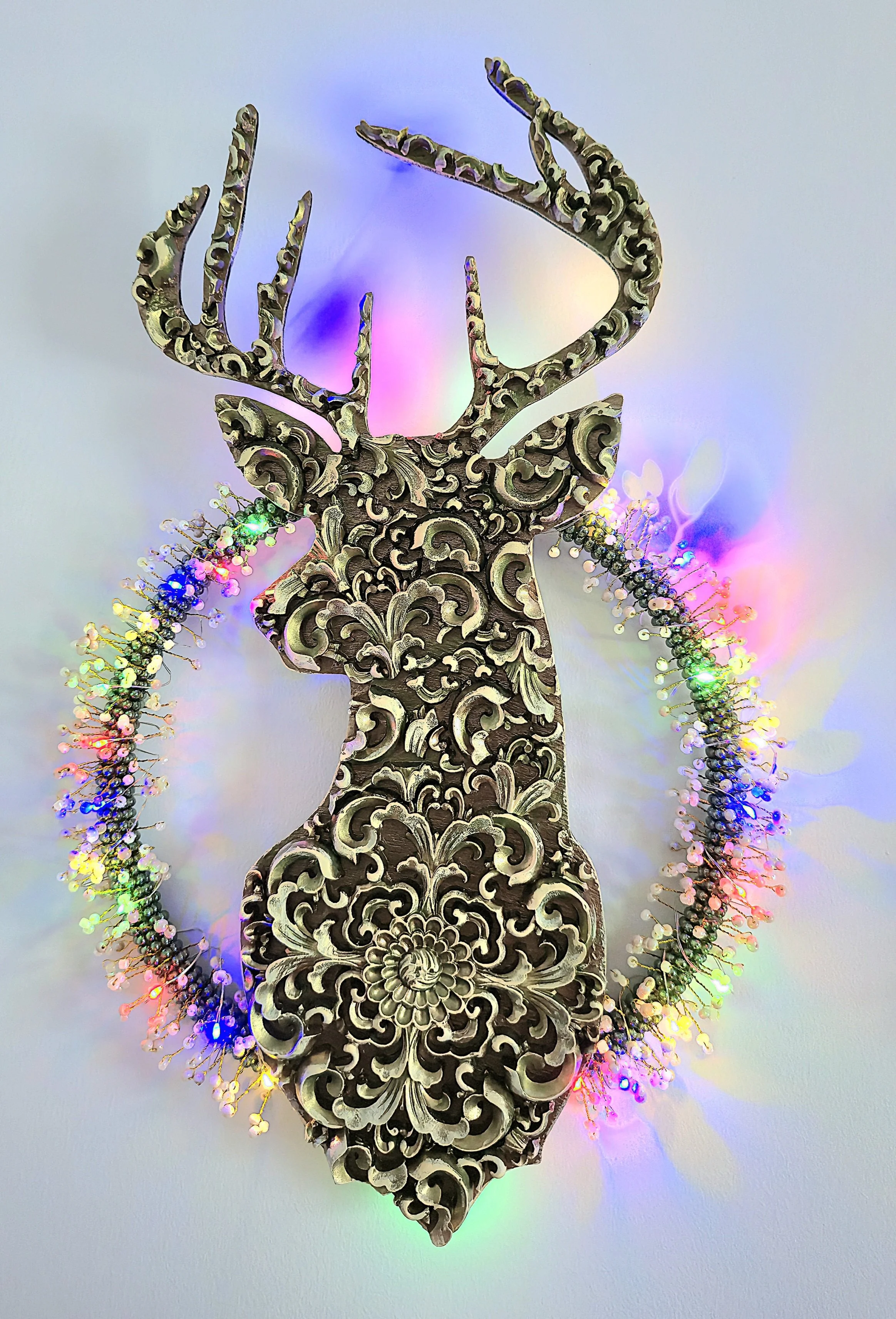 Décoration en forme de tête de cerf en bois sculpté, entourée d'une guirlande de lumières colorées.