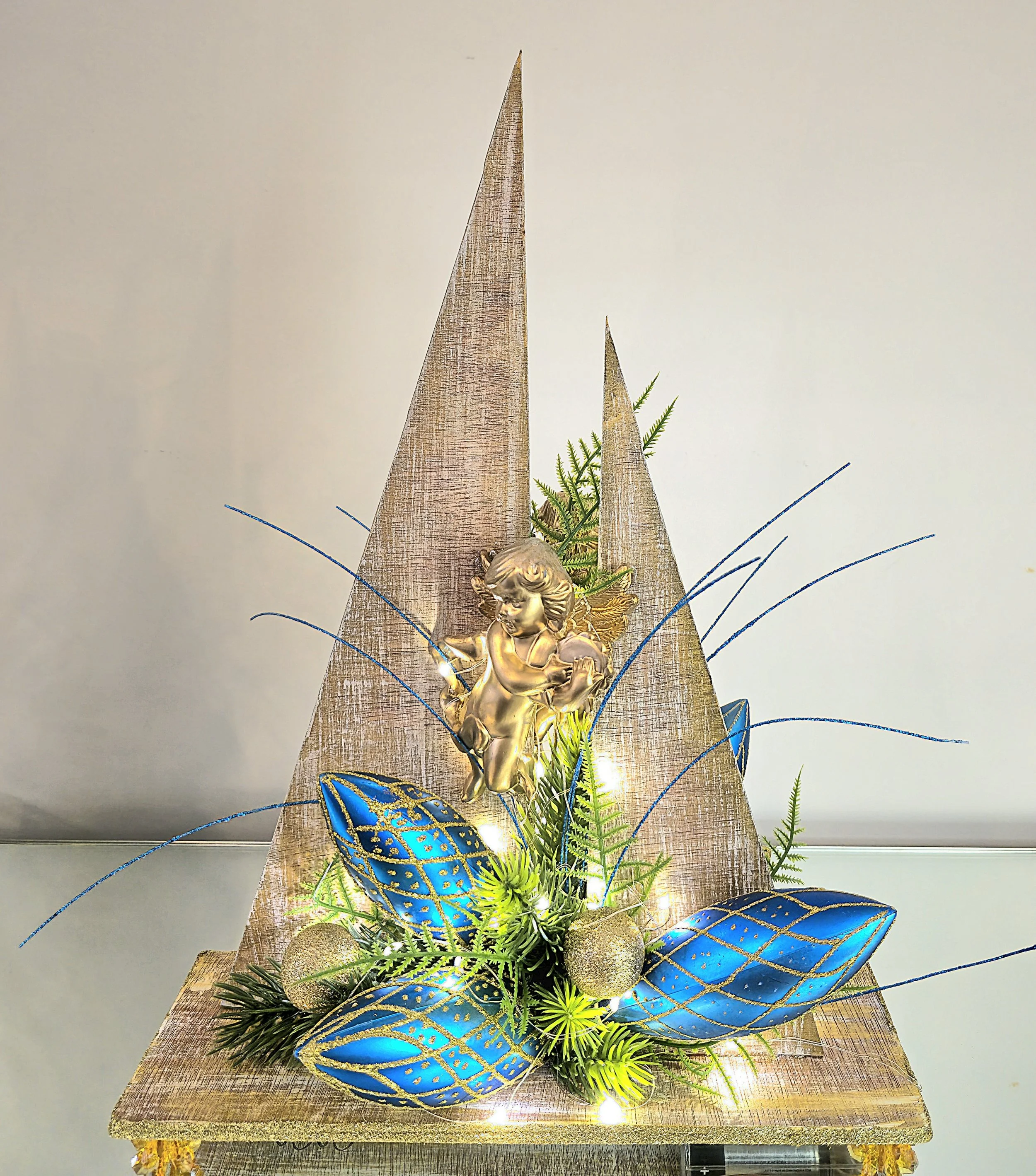 Décoration de Noël avec une sculpture d'ange doré, des feuilles bleu et or, des boules dorées, et des lumières.