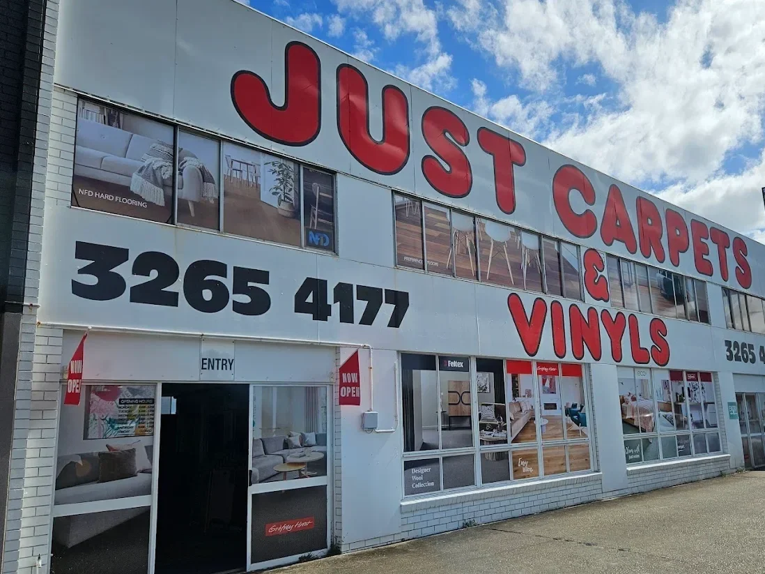 Exterior of a store named 'Just Carpets & Vinyls' with a large sign displaying the store's phone number and an open sign at the entrance.