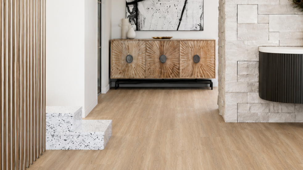 Interior view of a modern living space with light wood flooring, a wooden sideboard with circular metal accents, white vases on top, abstract black and white wall art, a white textured stone wall, and a black curved feature on the stone wall.