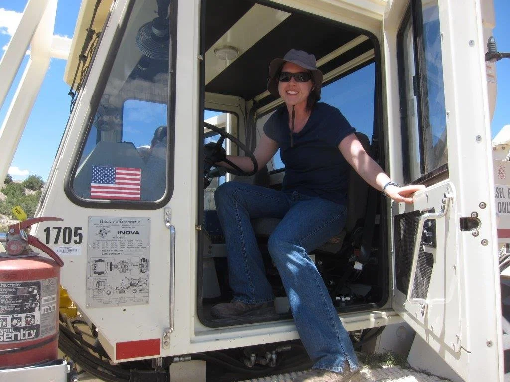 SAGE, Summer of Applied Geophysical Experience. A woman wearing a hat and sunglasses sits inside and leans out of a large equipment.