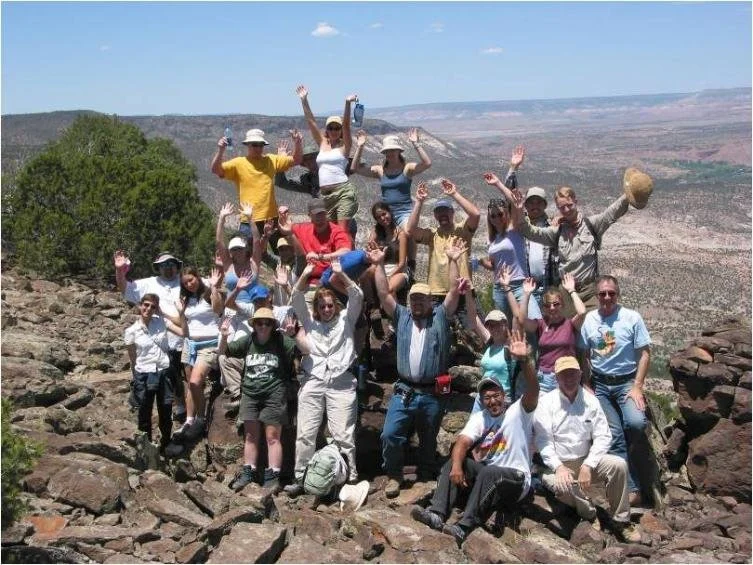 SAGE, Summer of Applied Geophysical Experience. Group of people posing on rocky terrain with a canyon in the background, raising their hands and smiling.