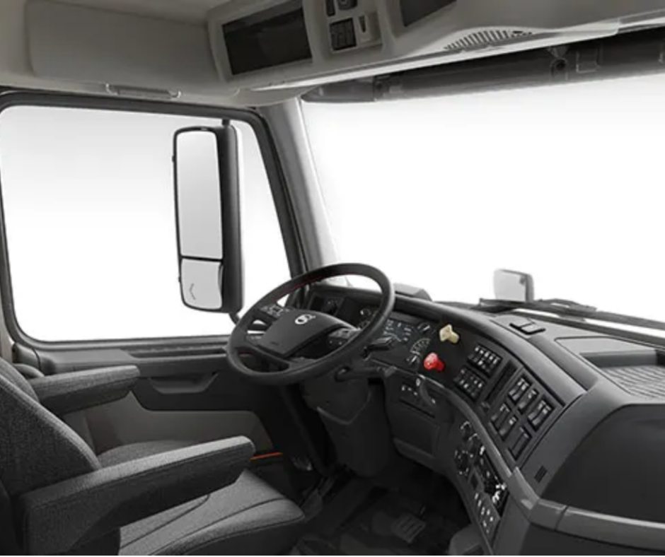Interior of a commercial truck cab with a steering wheel, driver’s seat, and dashboard controls.