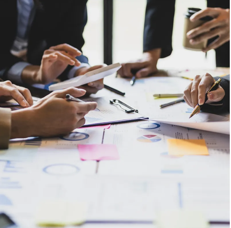 People collaborating around a table with documents, charts, and sticky notes, discussing and analyzing data.