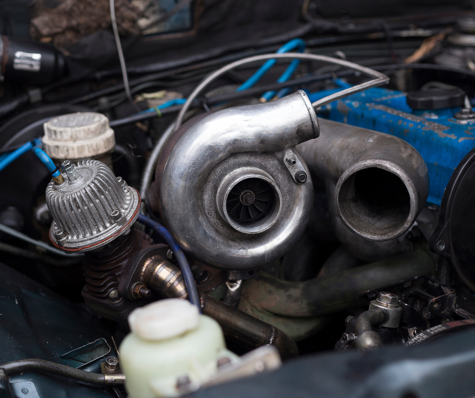 Close-up of a turbocharger installed in a car engine, with parts such as a blue engine block, hoses, and other engine components visible.