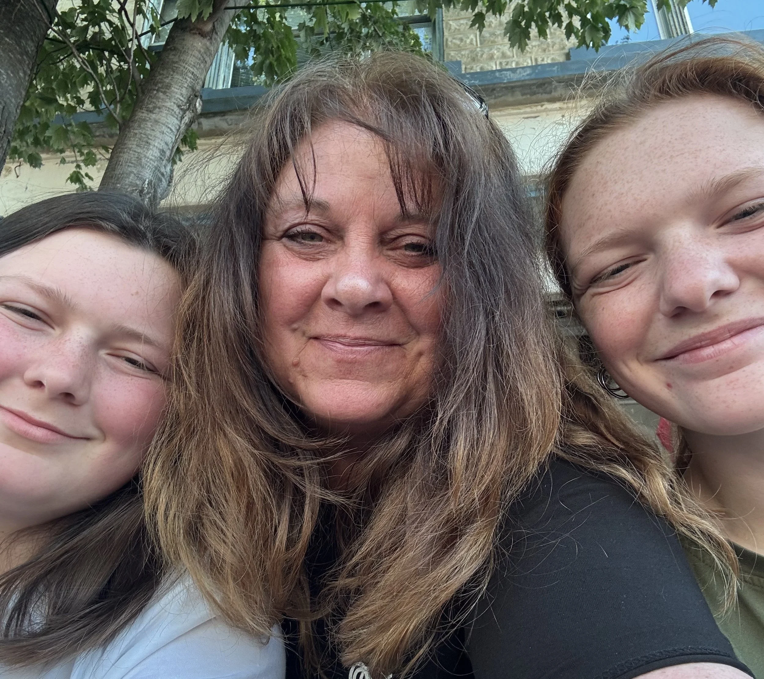 Three people taking a selfie outdoors, with trees and a building in the background.