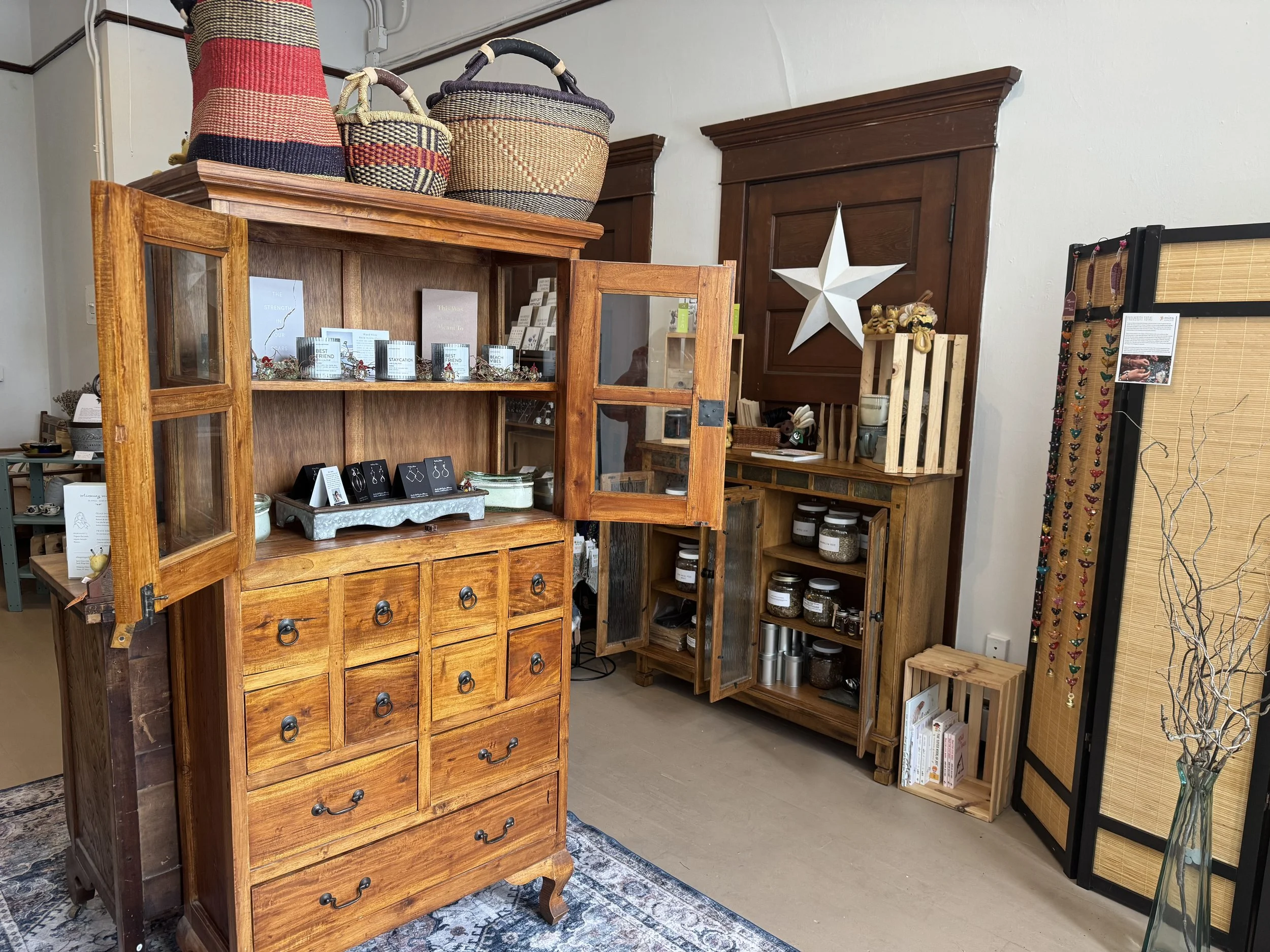 Interior of a shop showcasing wooden furniture and home decor items, including a large wooden cabinet with open doors, baskets on top, and a decorative star on the wall.