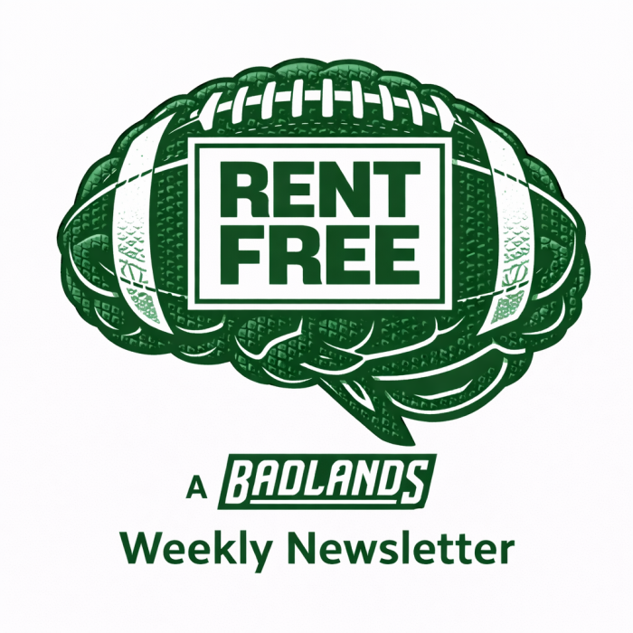 Wooden desk with vintage typewriter, green notebook, smartphone, pine cone, sunglasses, notepad, adhesive label, small bottle, and a branch.