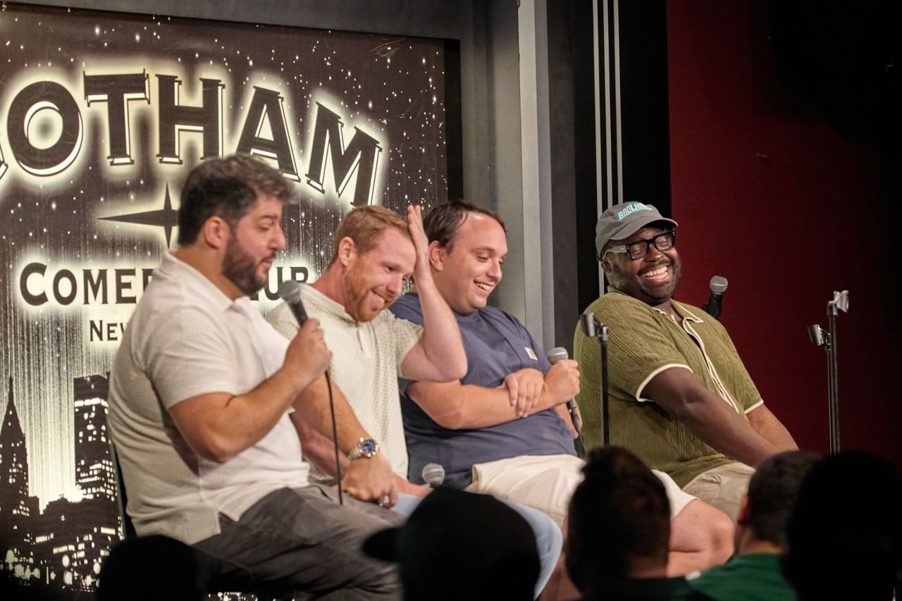 Four men sitting on a panel with microphones during a comedy event at Gotham Comedy Club in New York City.