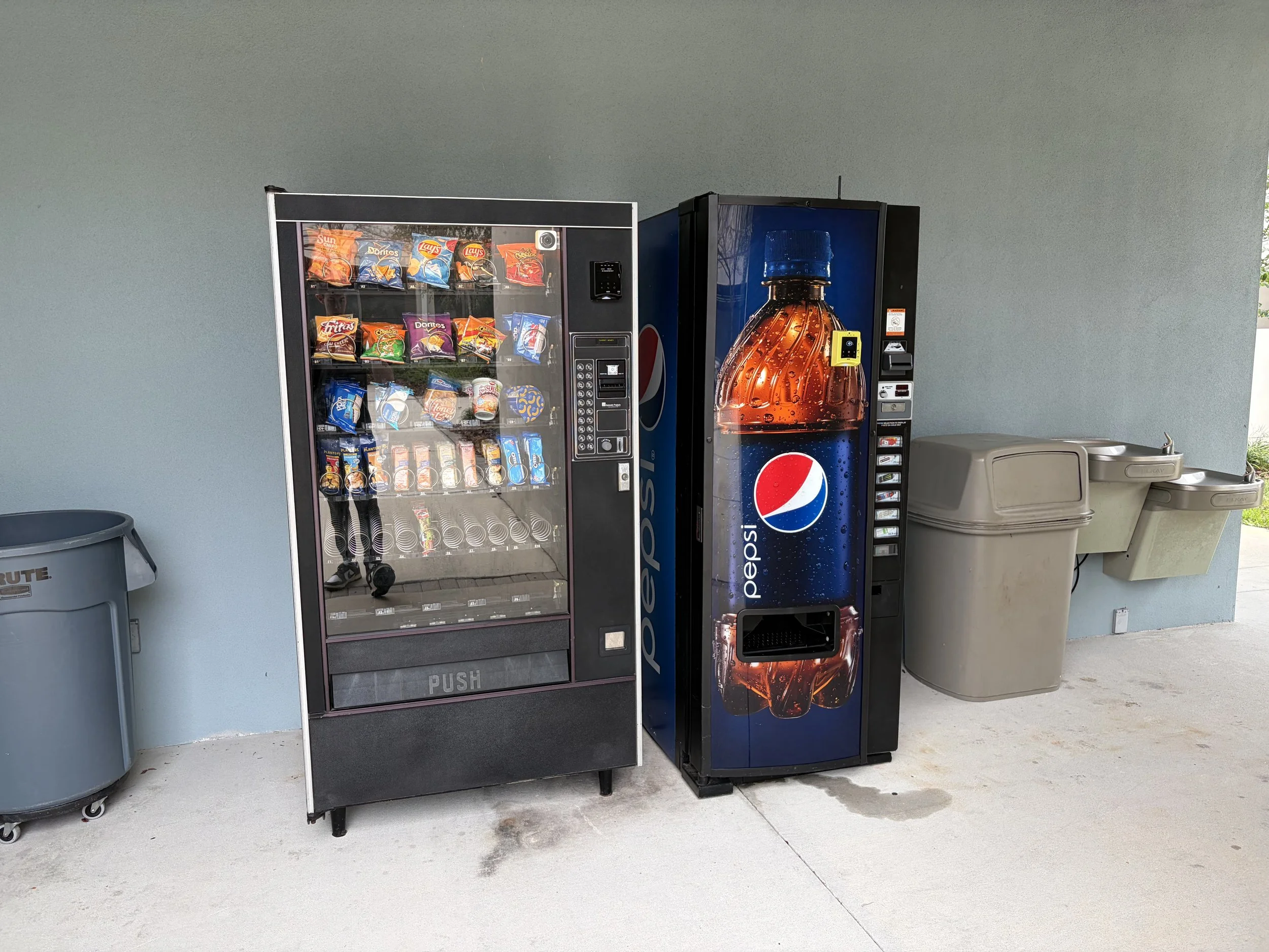 A vending machine stocked with various snack bags including Cheetos, Lay's, Doritos, Skittles, and Reese's, with a credit card reader on the right.
