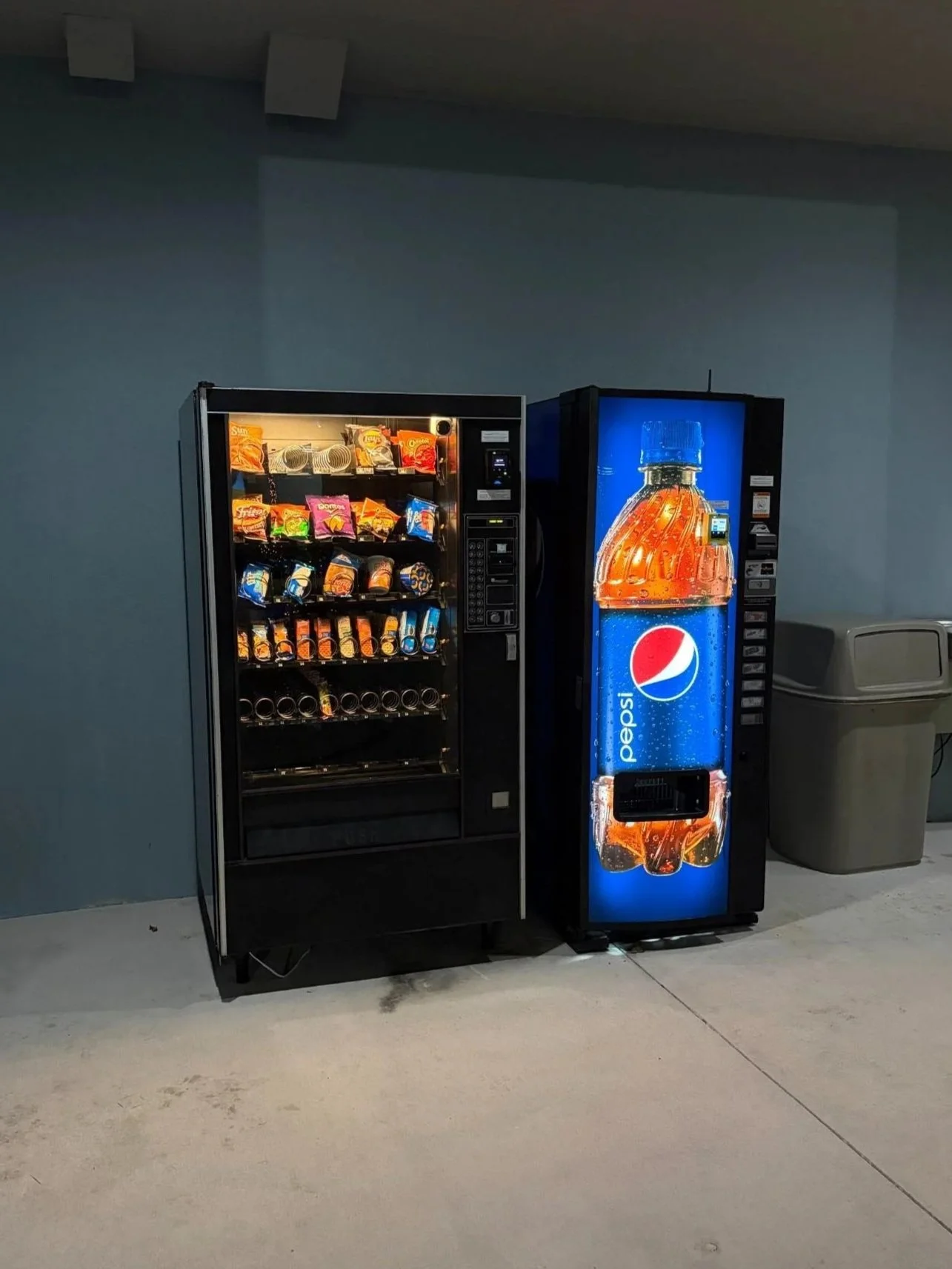 Vending machines for snacks and drinks against a light blue wall.