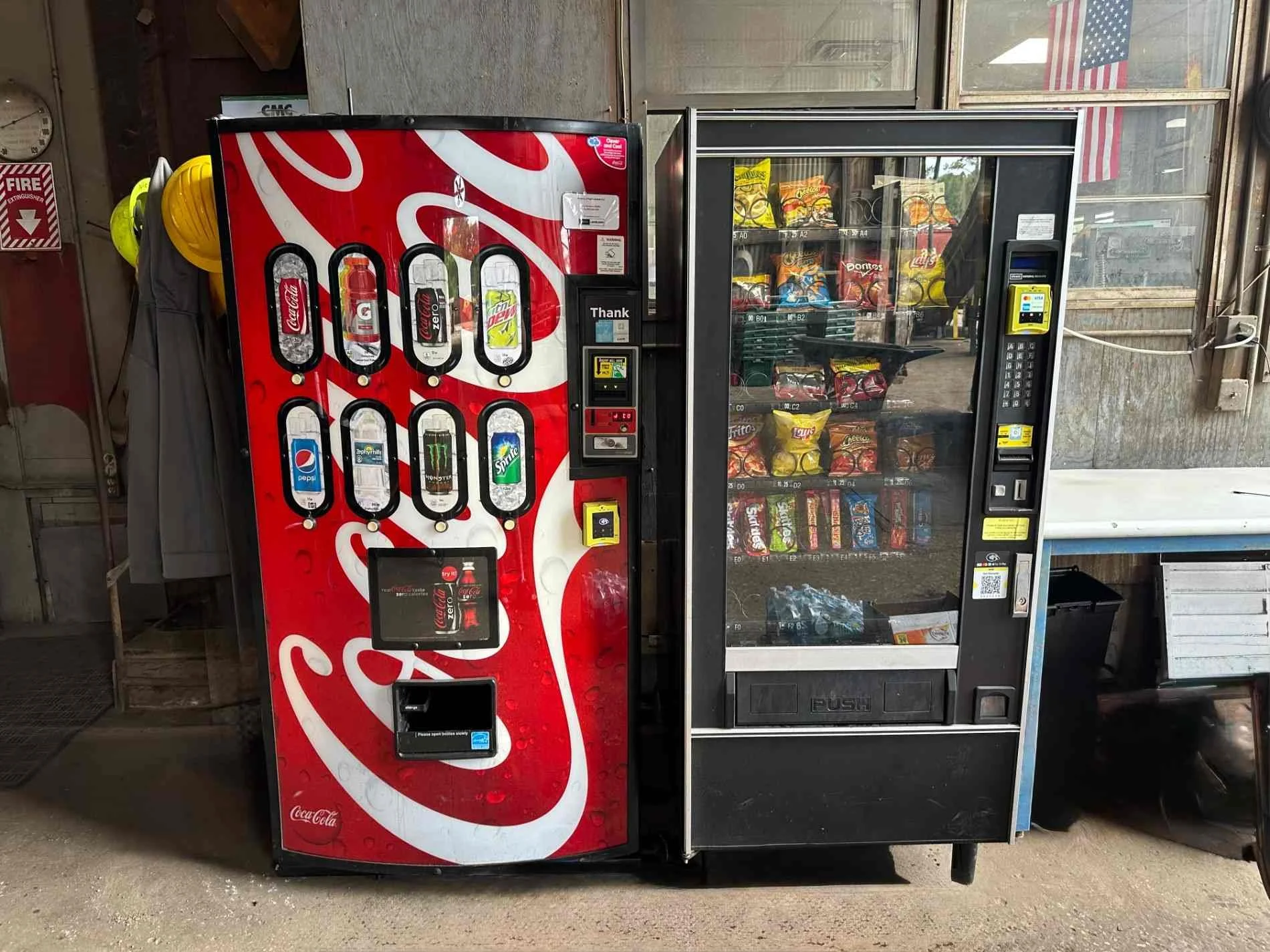 Two vending machines, the left one offers sodas such as Coca-Cola, Pepsi, 7UP, Sprite, Dr. Pepper, Monster, and others. The right machine contains snack items like chips and candy, with an American flag seen through the window above the machines.