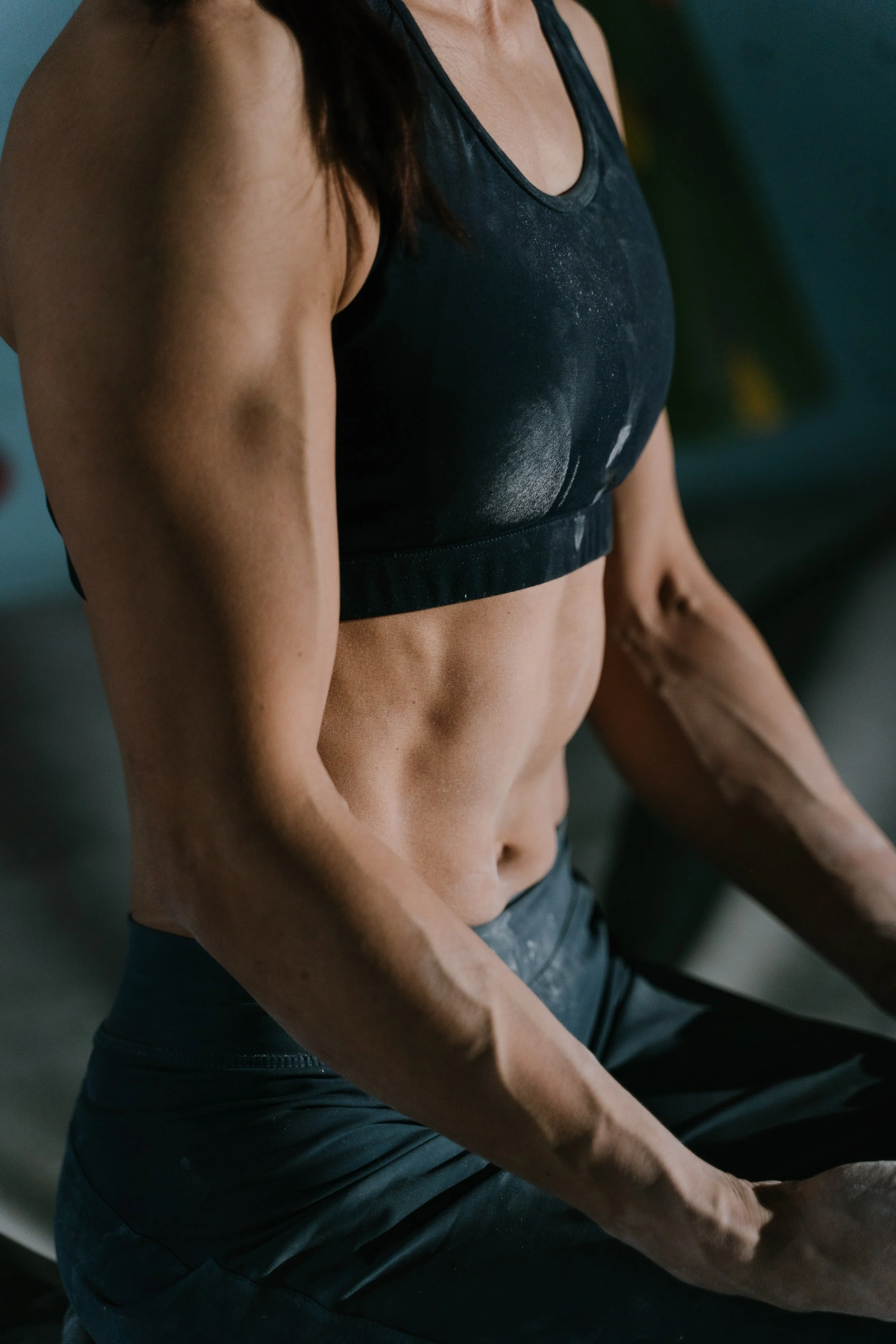 Close-up of a woman's toned abdomen and arm, wearing a black sports bra and workout pants.