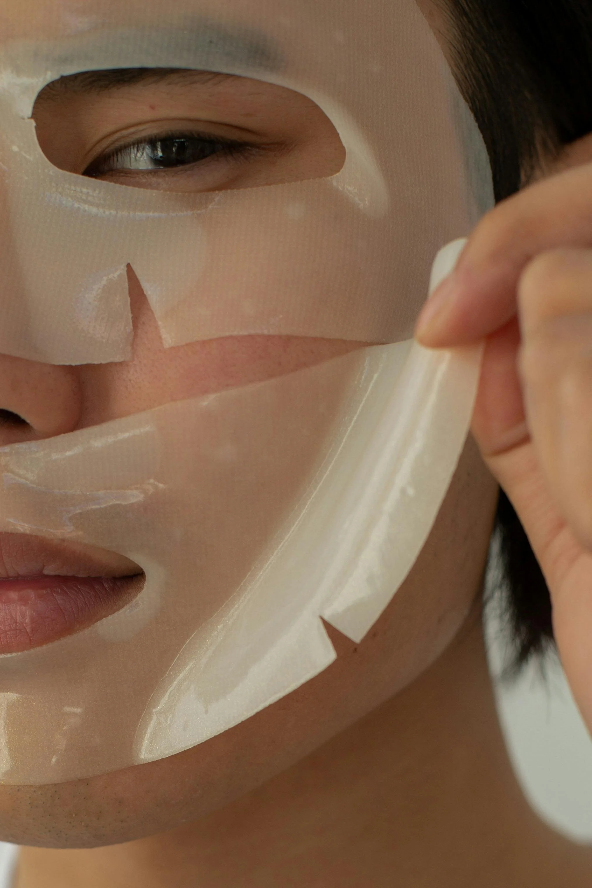 Close-up of a person peeling off a white sheet mask from their face.