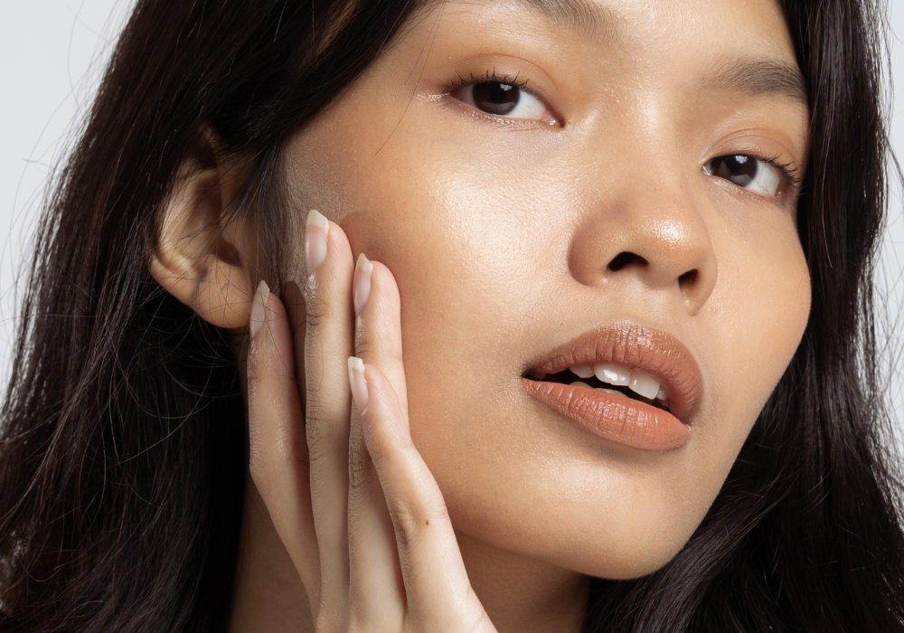 Close-up of a woman with brown hair applying skincare to her face with her hand.