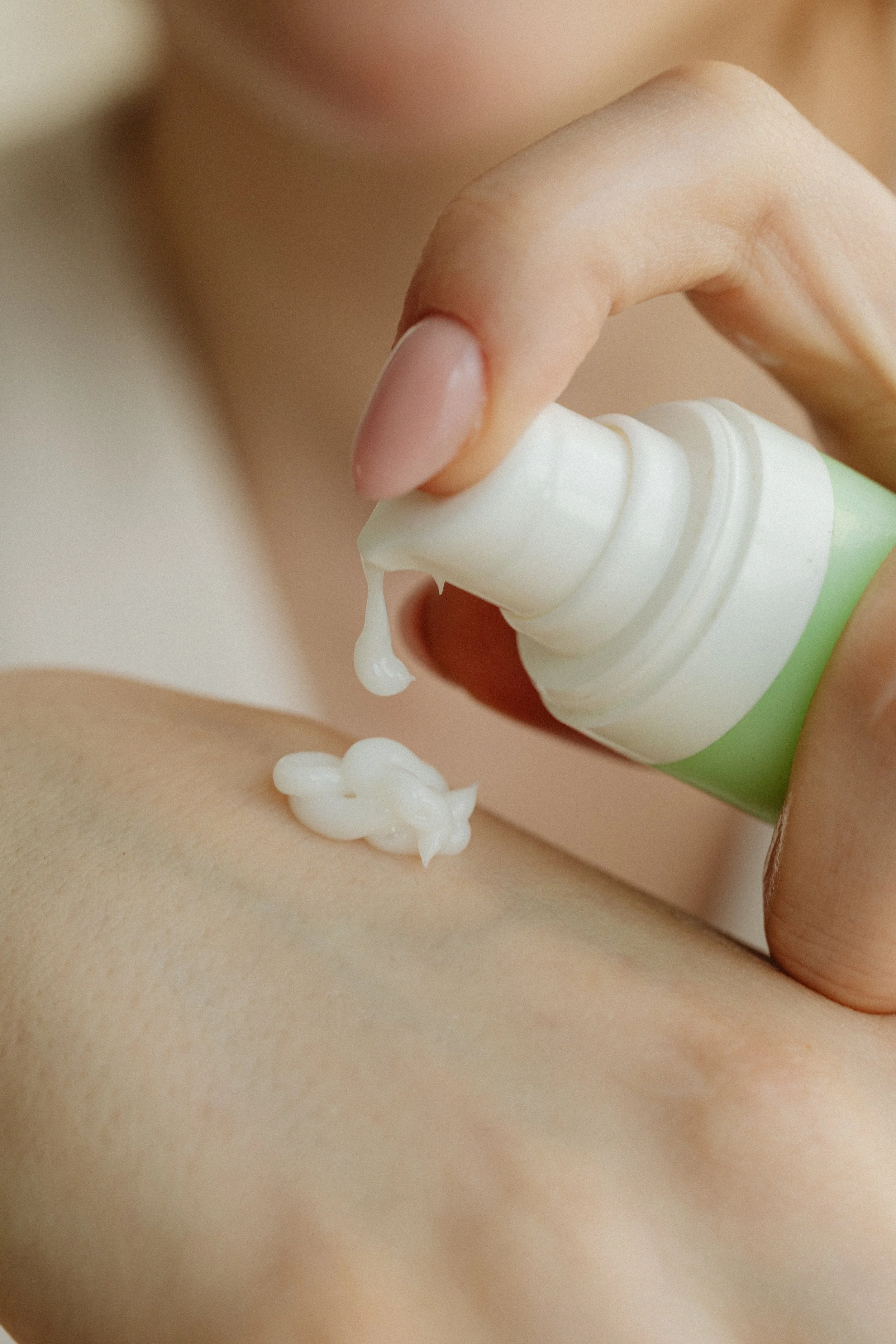 A person squeezing lotion or cream from a tube onto their skin.