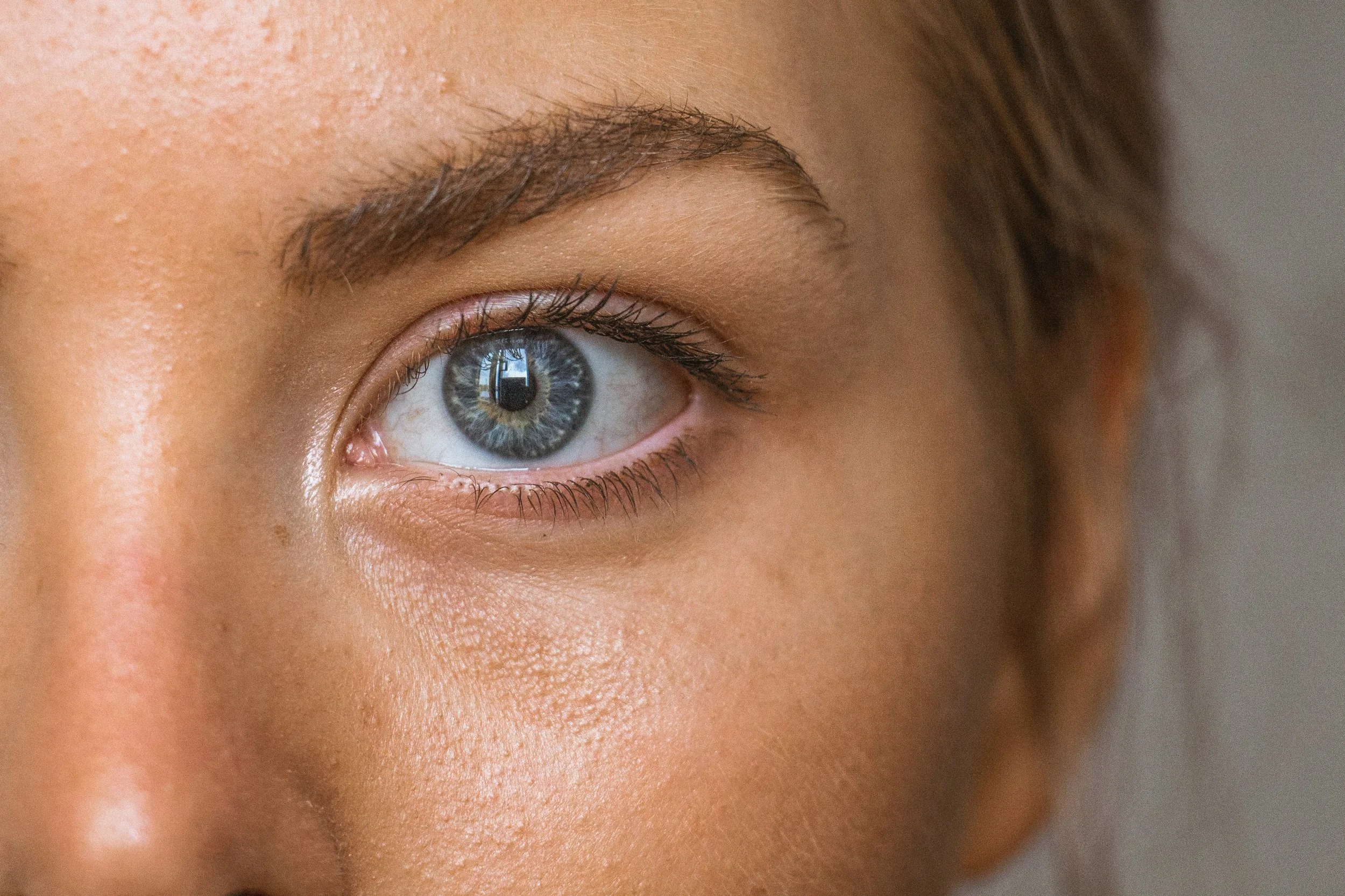 Close-up of a person's right eye with blue iris, reflected window, and surrounding facial features.