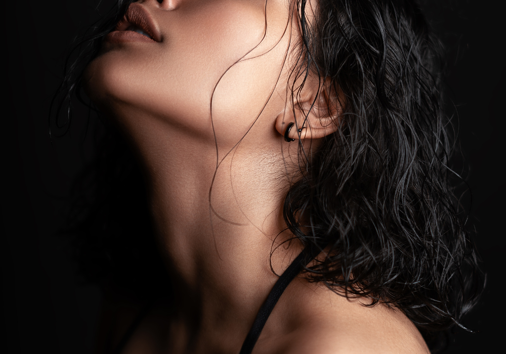 Close-up of a woman's neck, part of her face, and her curly black hair, with her lips slightly parted.