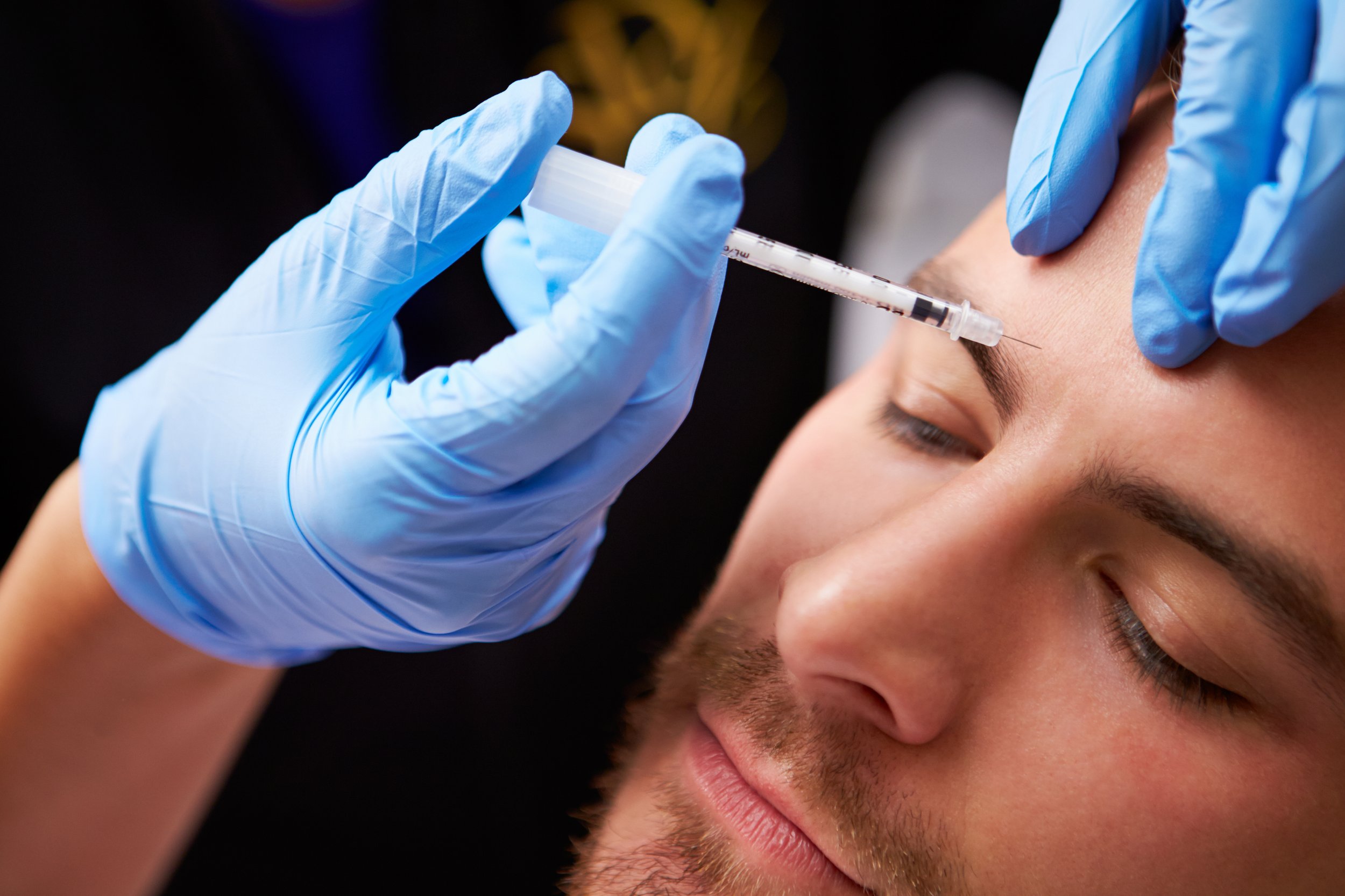 Person receiving a cosmetic injection in the forehead from a medical professional wearing blue gloves.