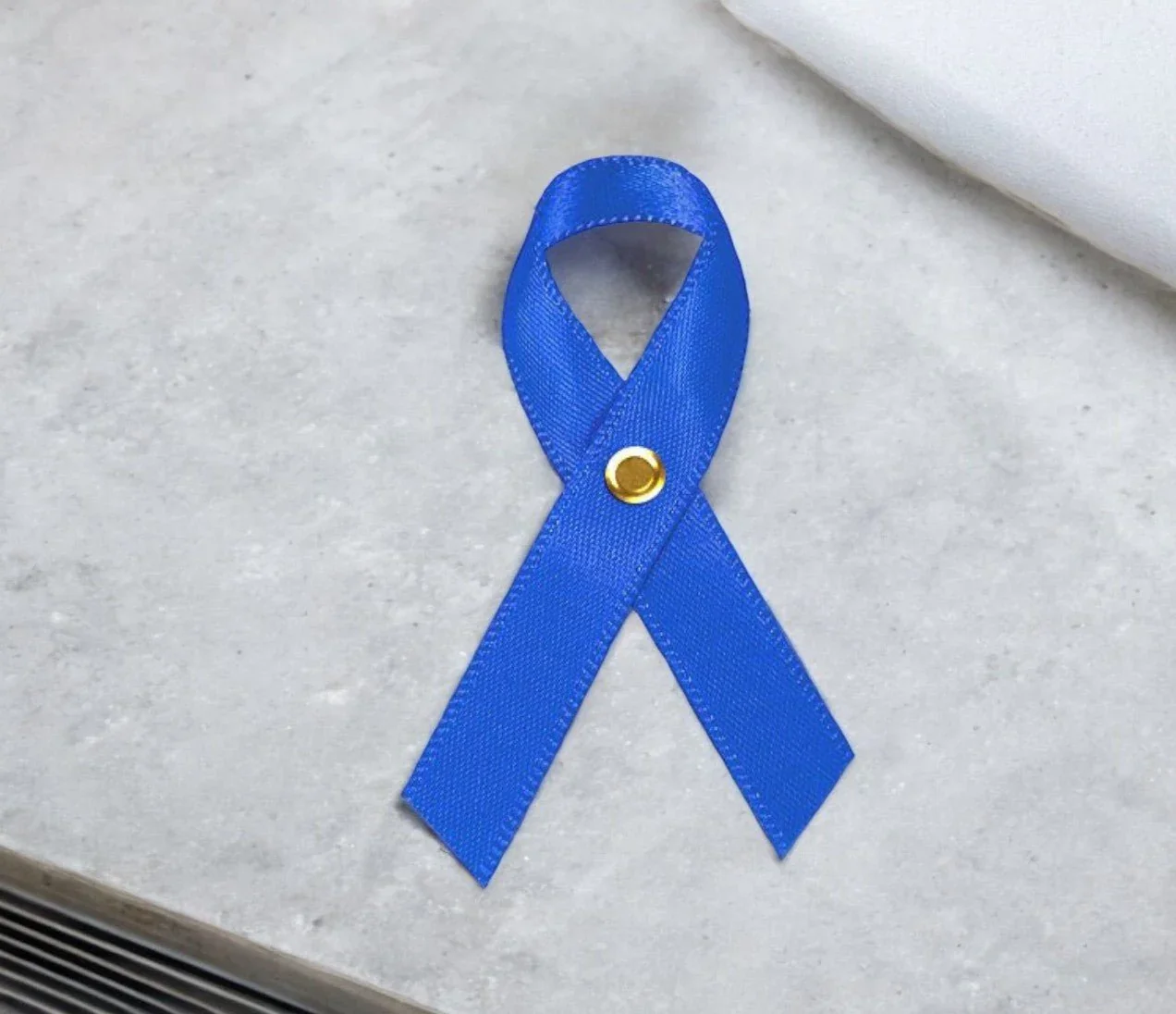 Blue awareness ribbon with a gold eyelets on a white surface.