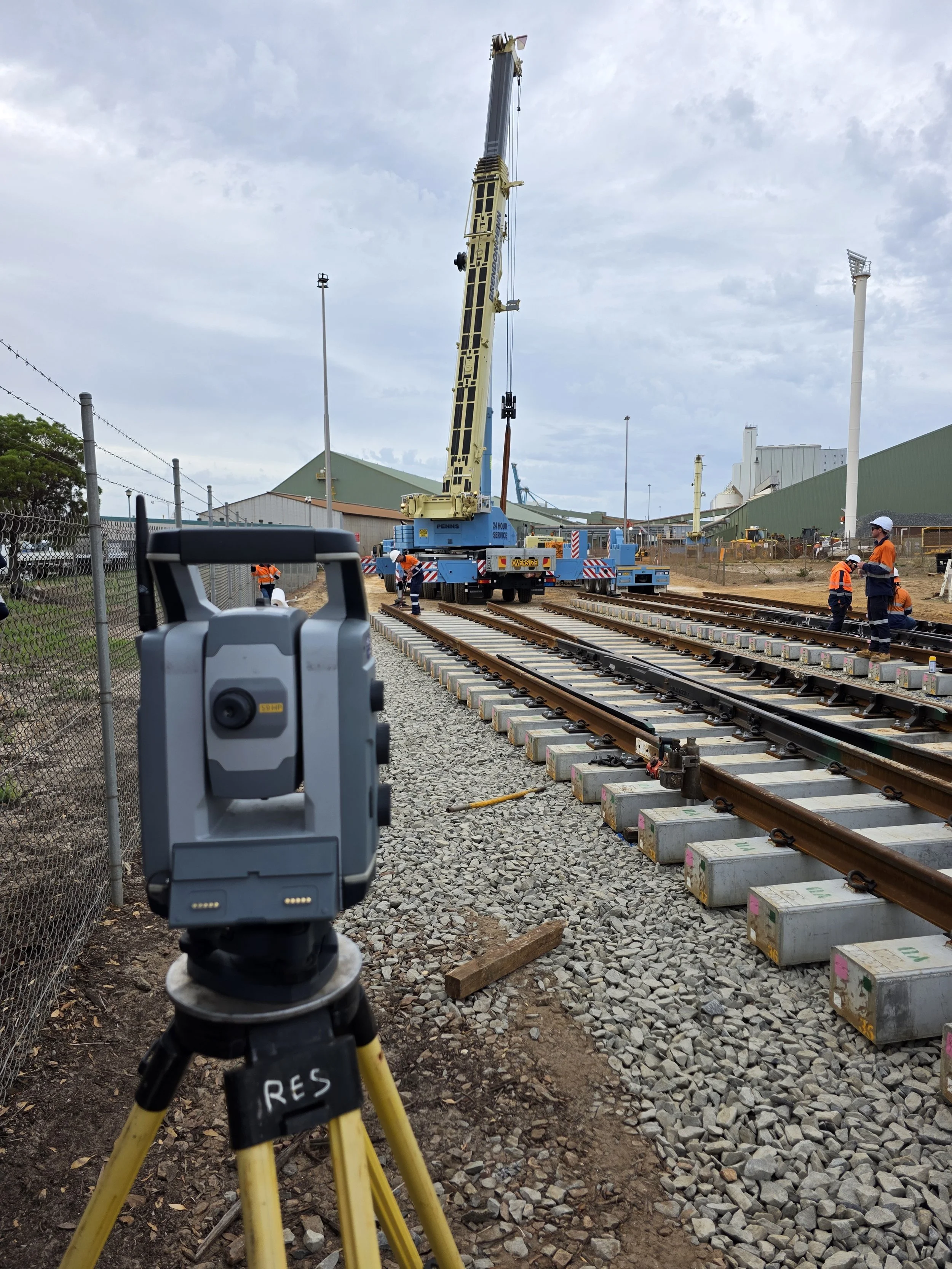 Construction workers and a crane working on railroad track installation at a construction site.