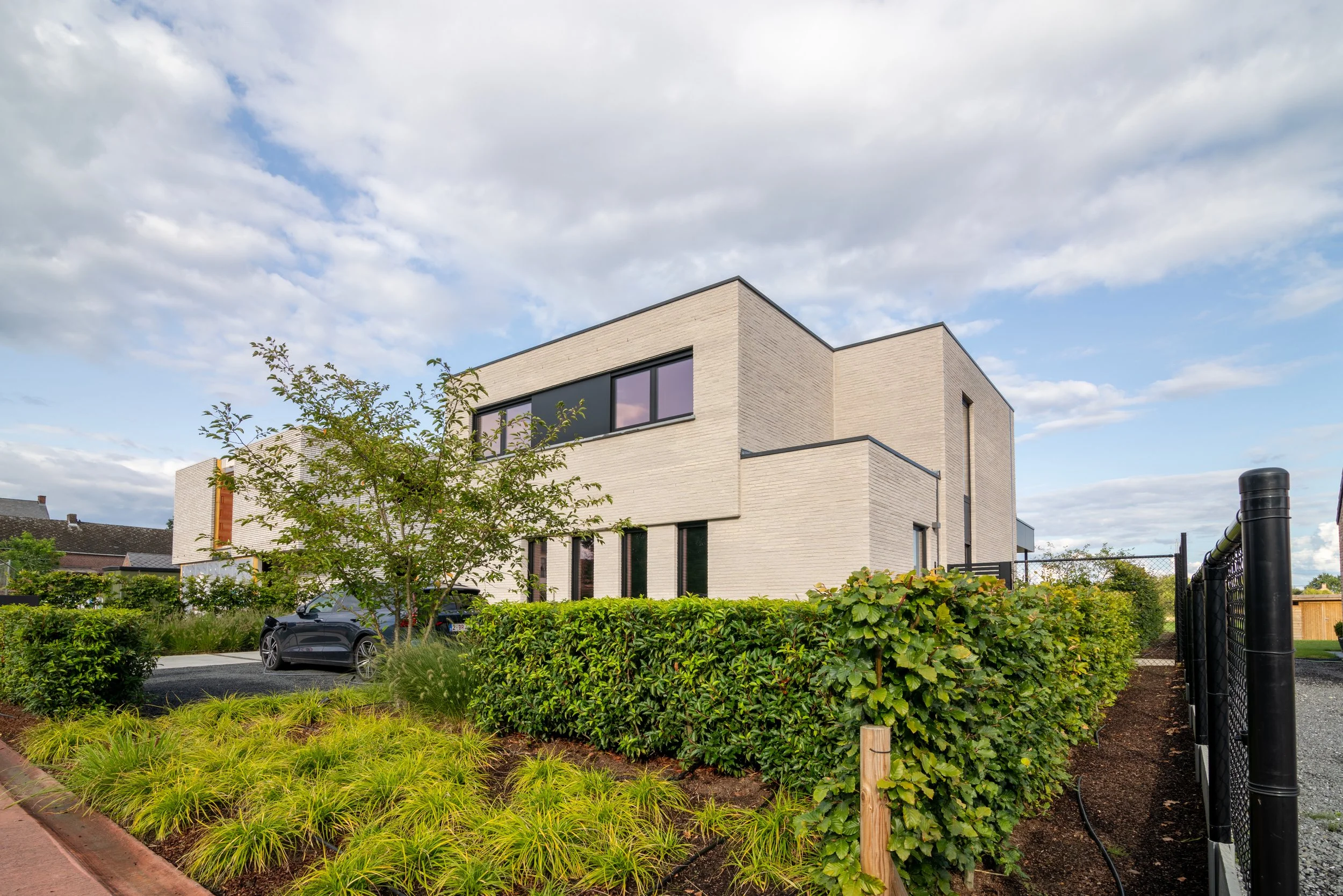 Strakke voortuin met groene hagen en siergrassen rond moderne woning, ontworpen door Tuinarchitect Florian