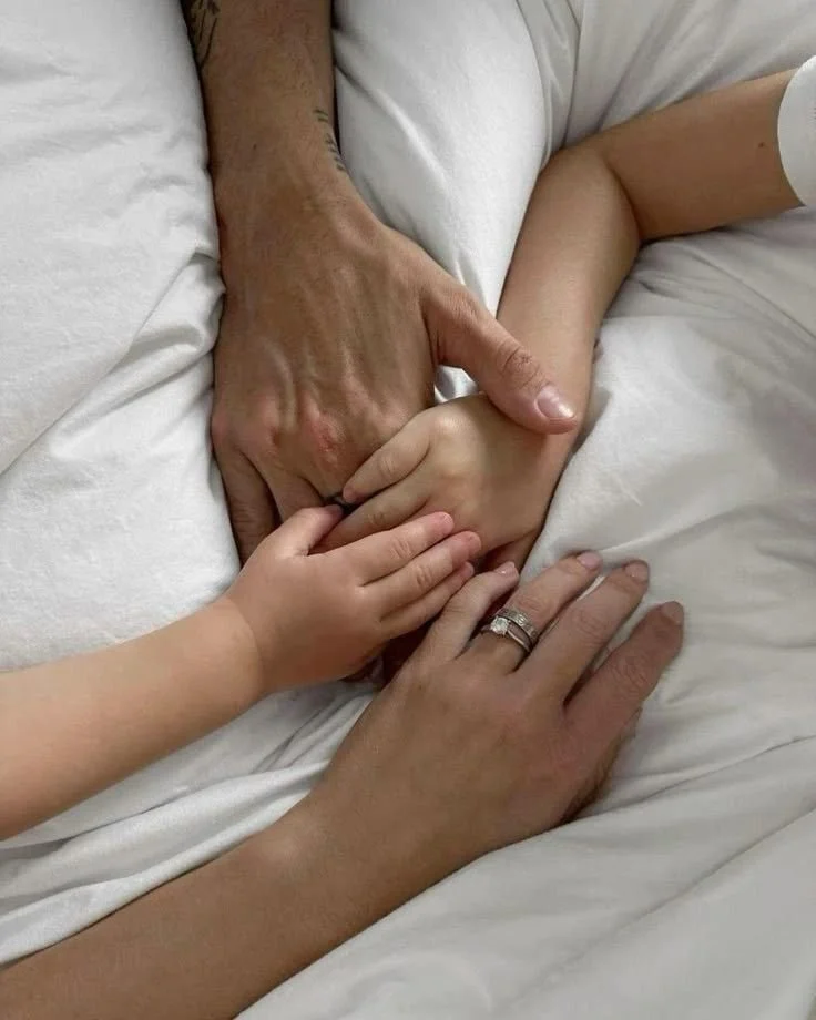 A man, woman, and child holding hands on a bed.